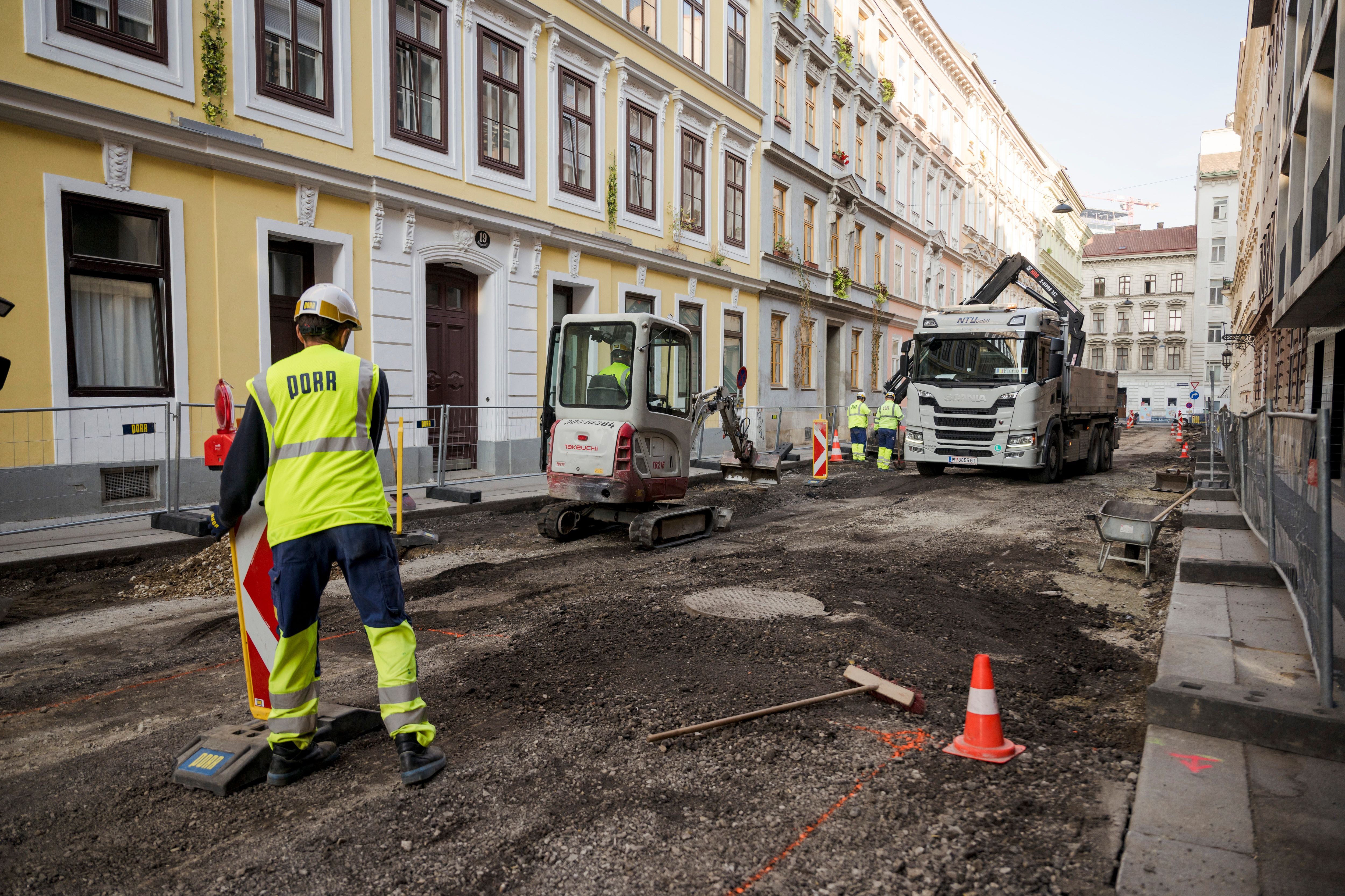 Straßenbauarbeiten mit Bauarbeitern, Bagger und LKW in der Rüdigergasse einer Wohngegend.
