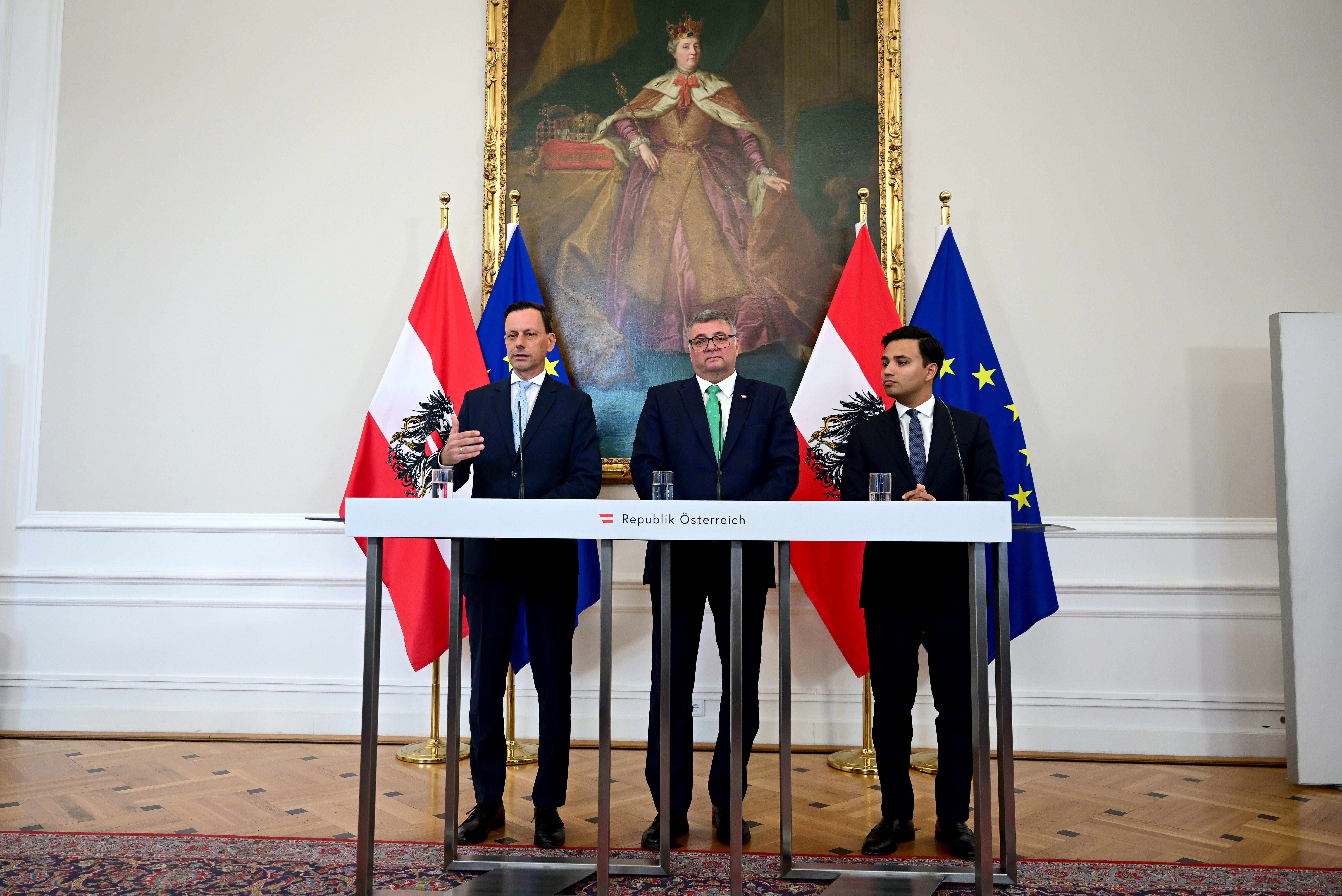 Drei Männer bei einer Pressekonferenz vor österreichischen und EU-Flaggen in Wien.