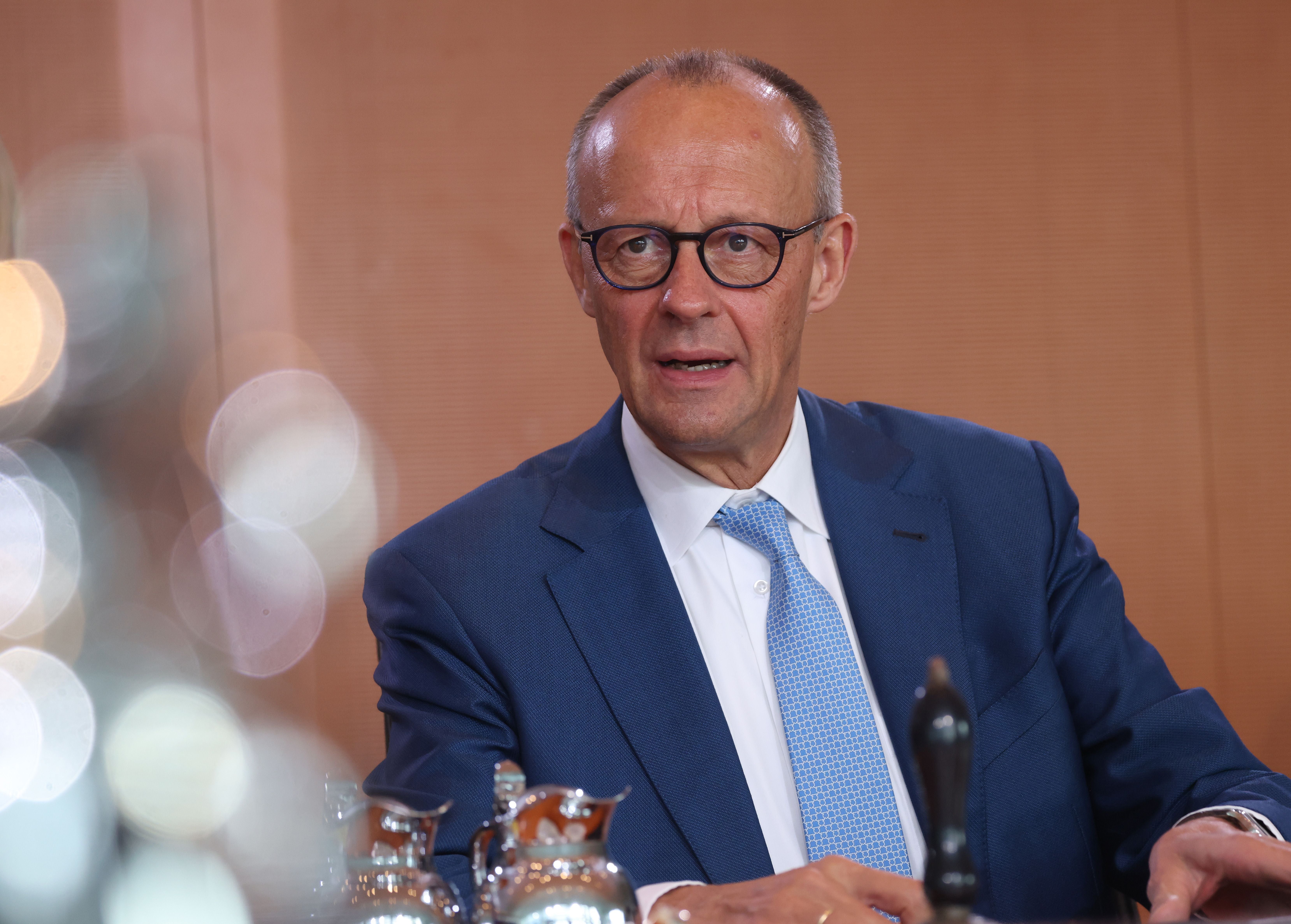Ein Mann im blauen Anzug und mit Brille sitzt an einem Tisch vor verschwommenem Hintergrund.