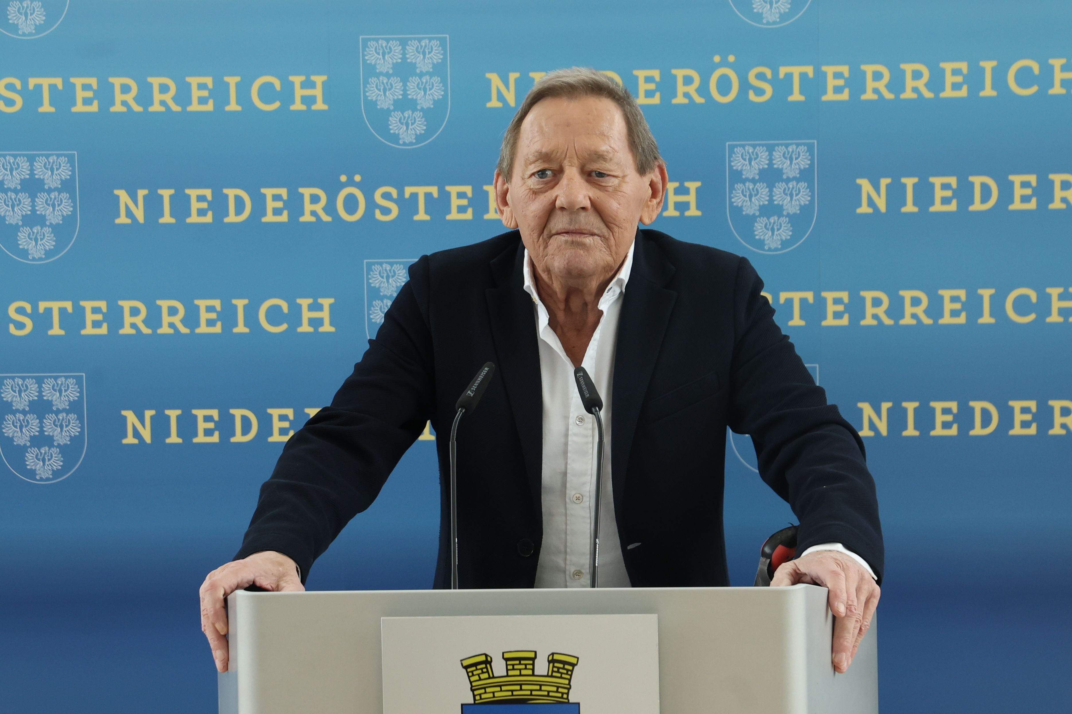 Mann im Anzug spricht am Rednerpult vor einer Wand mit Niederösterreich-Logos.