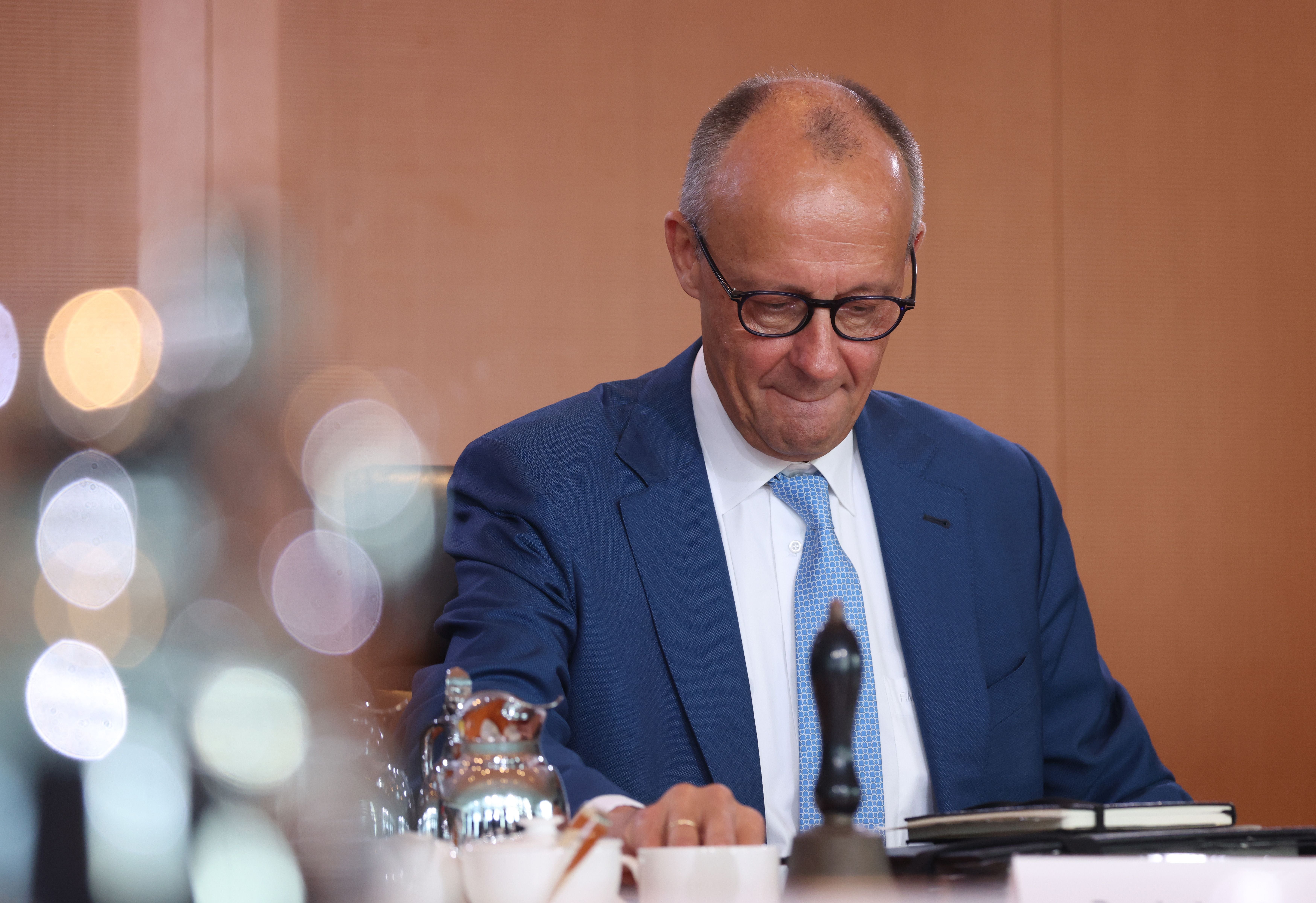 Ein Mann im blauen Anzug und mit Brille sitzt an einem Tisch und blickt nach unten.