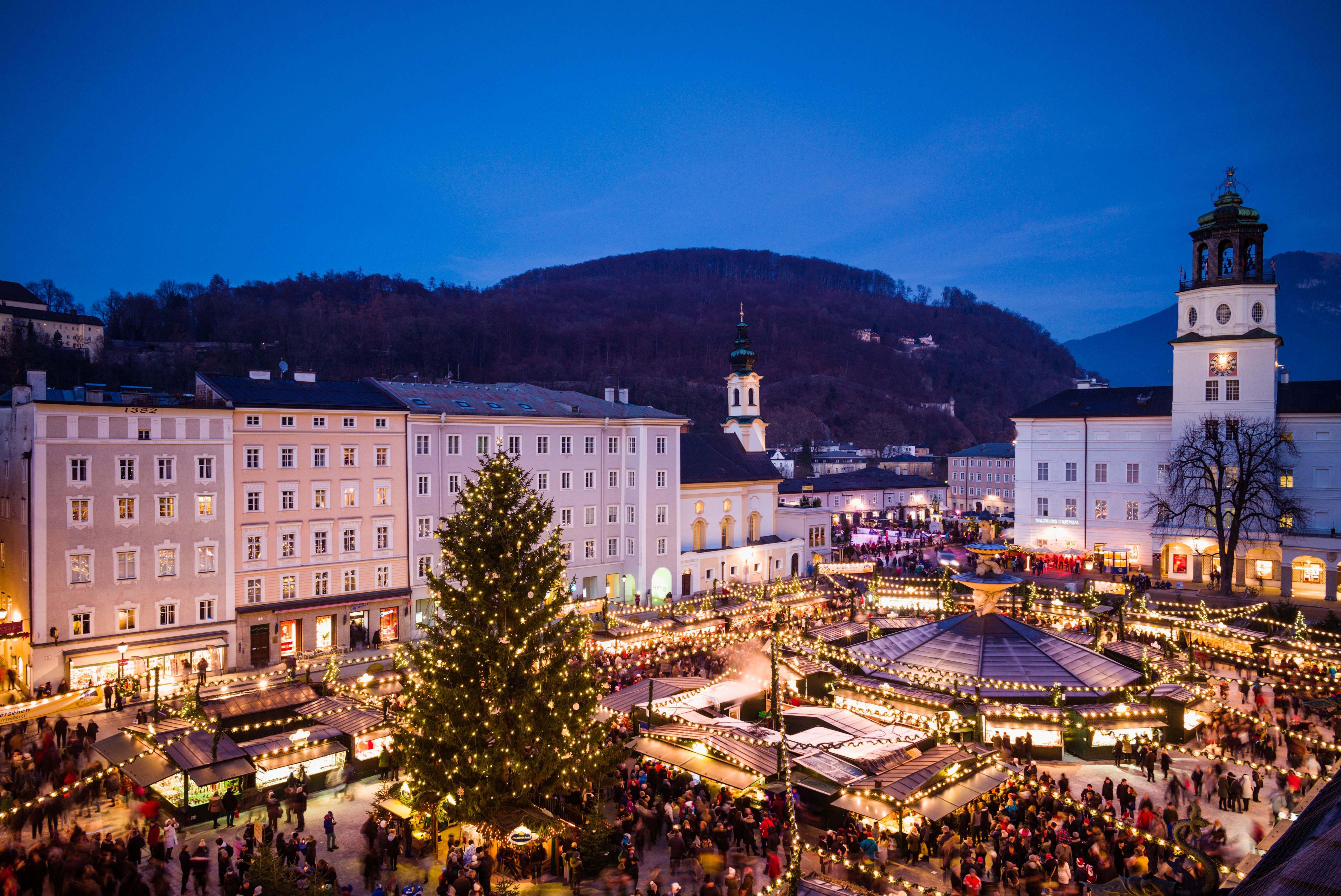 Blick auf den festlich beleuchteten Salzburger Christkindlmarkt am Residenzplatz bei Dämmerung.