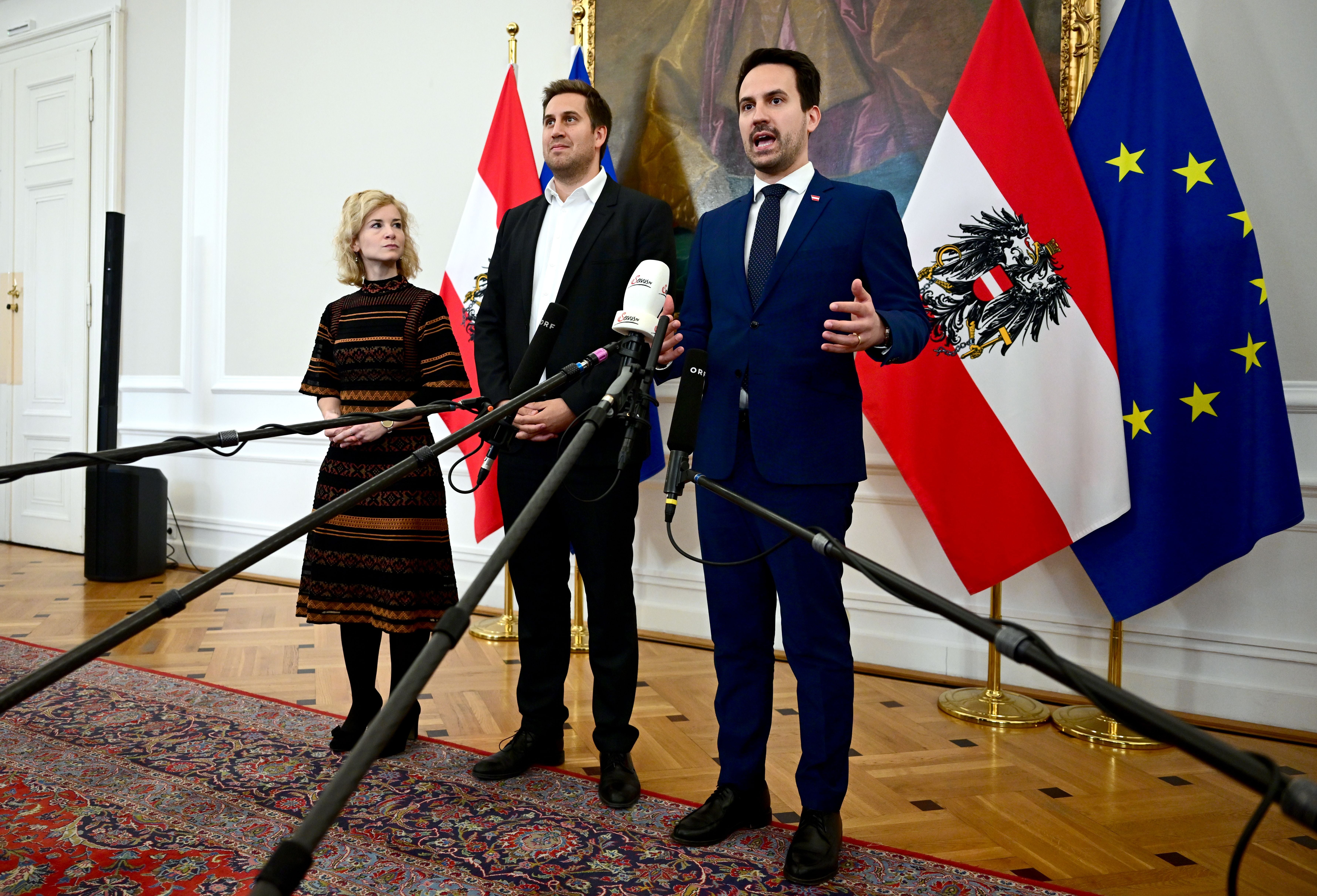 Drei Personen sprechen bei einer Pressekonferenz vor österreichischer und EU-Flagge in Wien.