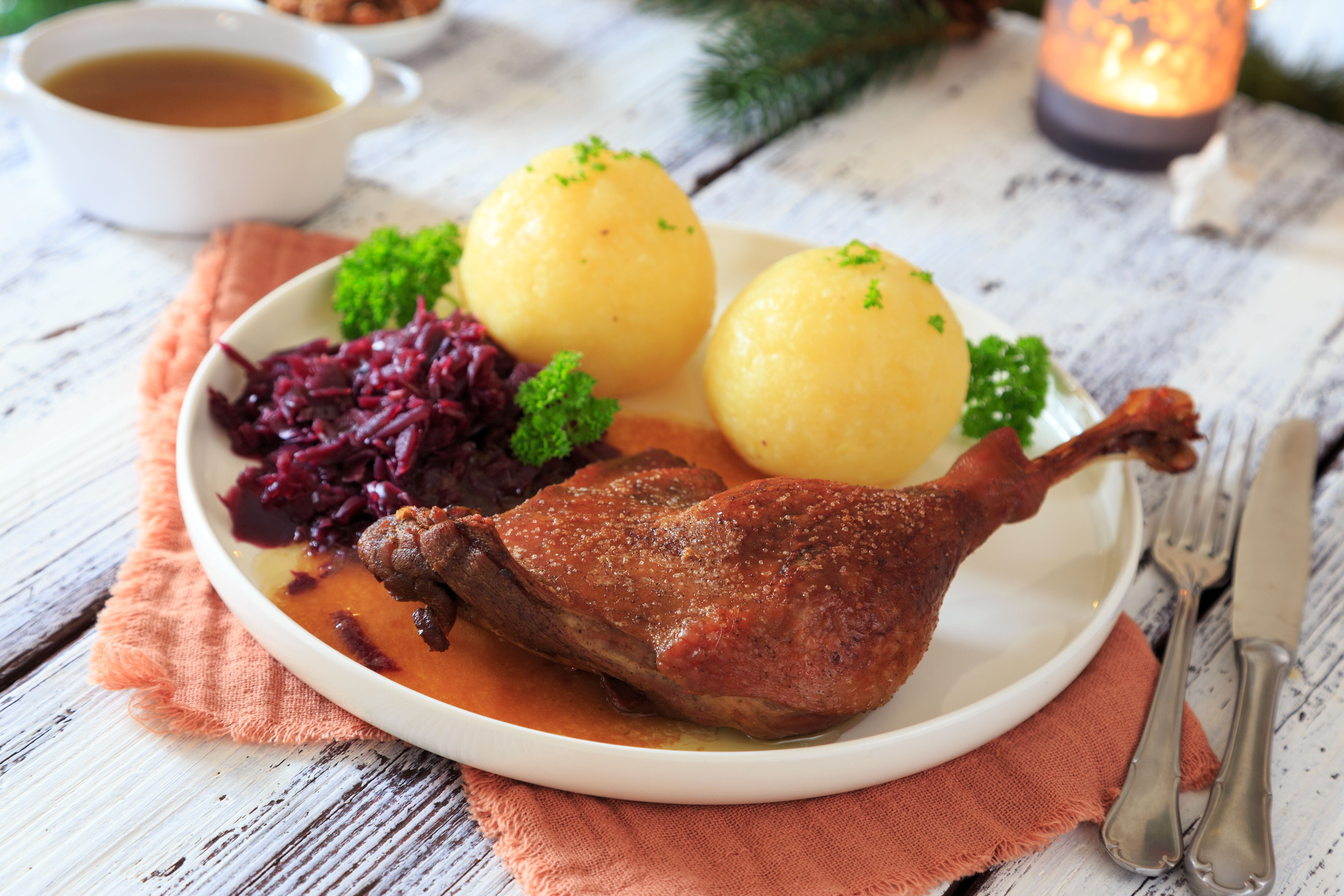 Gänsekeule mit Rotkohl und zwei Kartoffelklößen auf einem weißen Teller serviert.