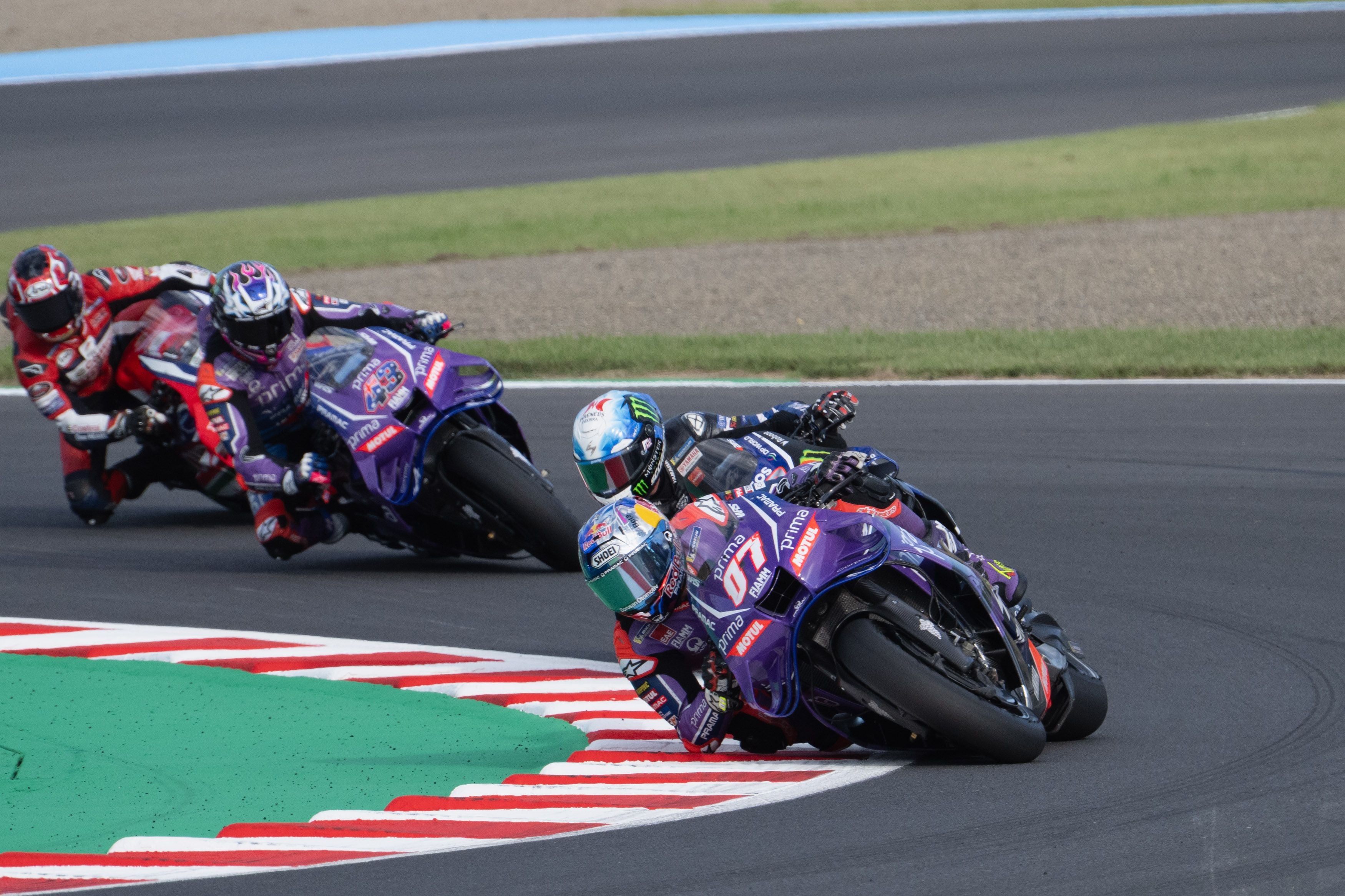 Drei MotoGP-Fahrer in voller Montur lehnen sich mit ihren Rennmaschinen eng aneinander in eine scharfe Kurve.
