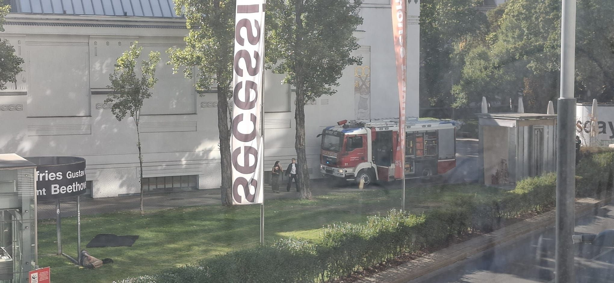 Feuerwehrauto steht vor einem Museumsgebäude, Menschen gehen auf dem Gehweg entlang.