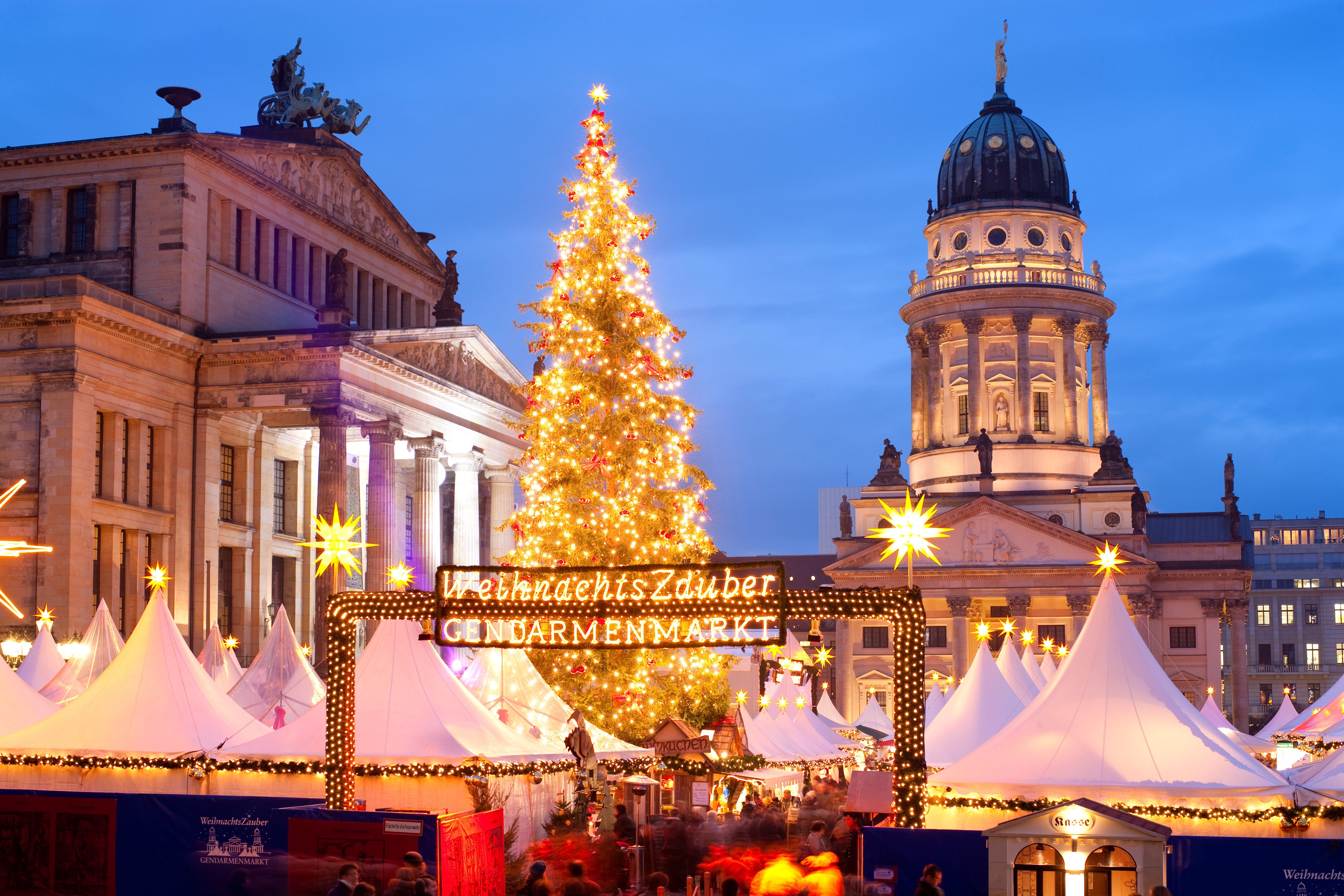 Beleuchteter Weihnachtsmarkt mit großem Weihnachtsbaum am Gendarmenmarkt in Berlin bei Abenddämmerung.