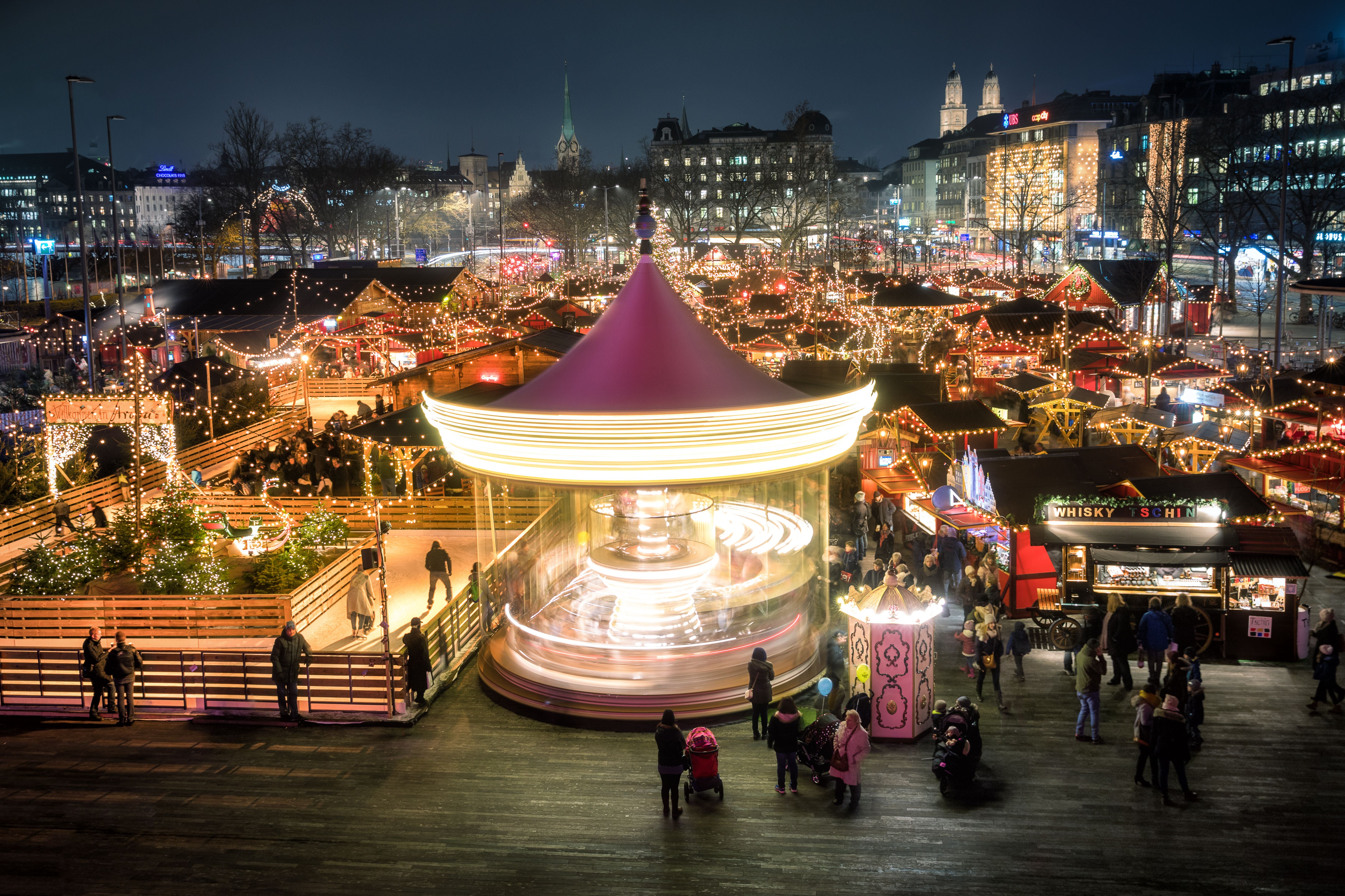 Weihnachtsmarkt in Zürich bei Nacht mit beleuchtetem Karussell und vielen dekorierten Buden.