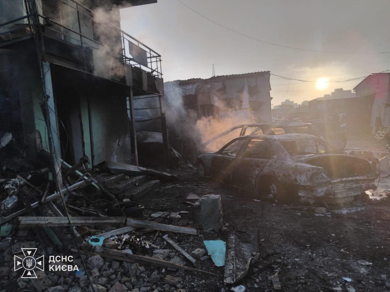 Ausgebranntes Auto, Trümmer und beschädigtes Gebäude nach einem Angriff in Kiew bei Sonnenuntergang.