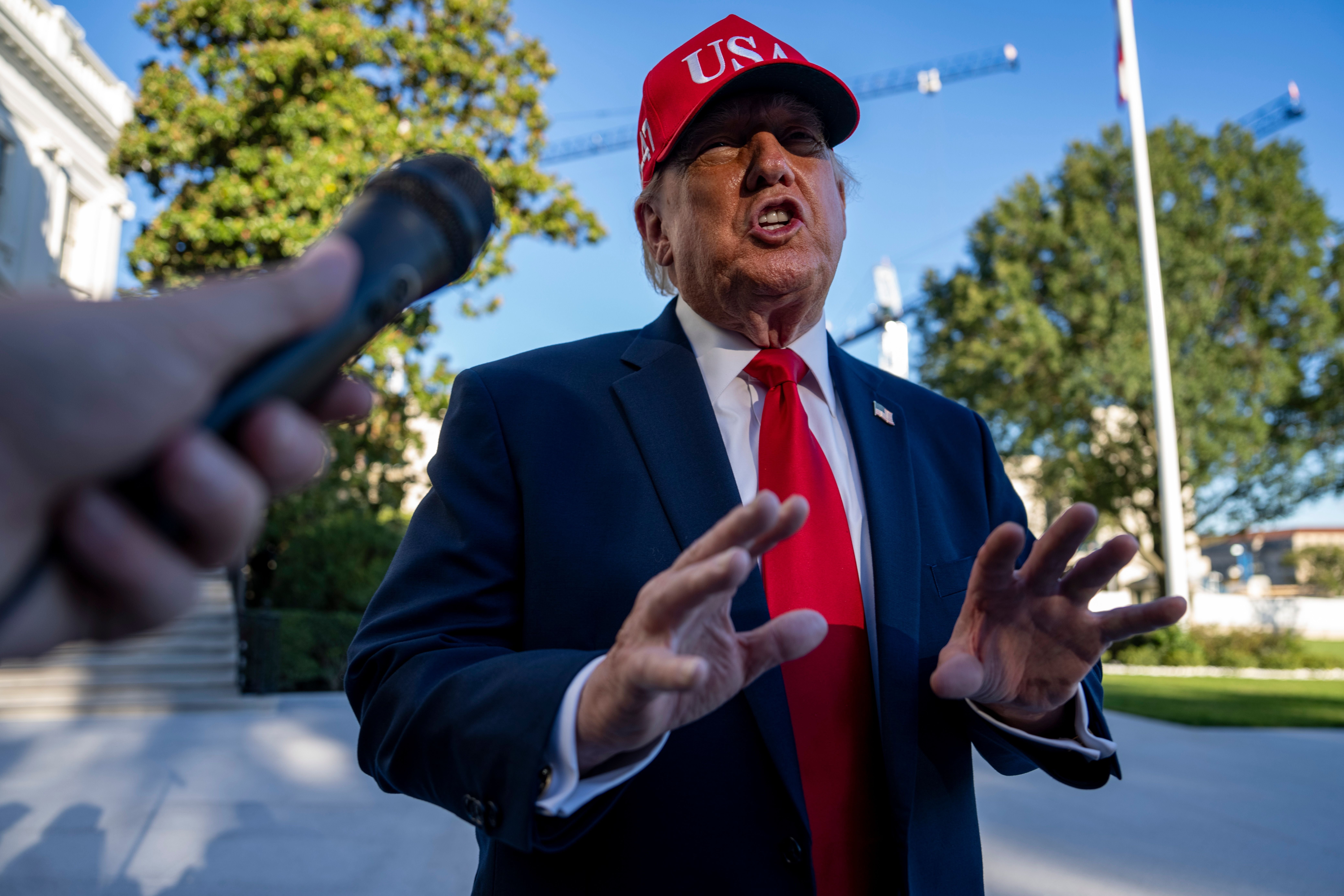 Ein Mann mit roter "USA"-Kappe spricht im Freien vor einem Mikrofon mit Reportern.