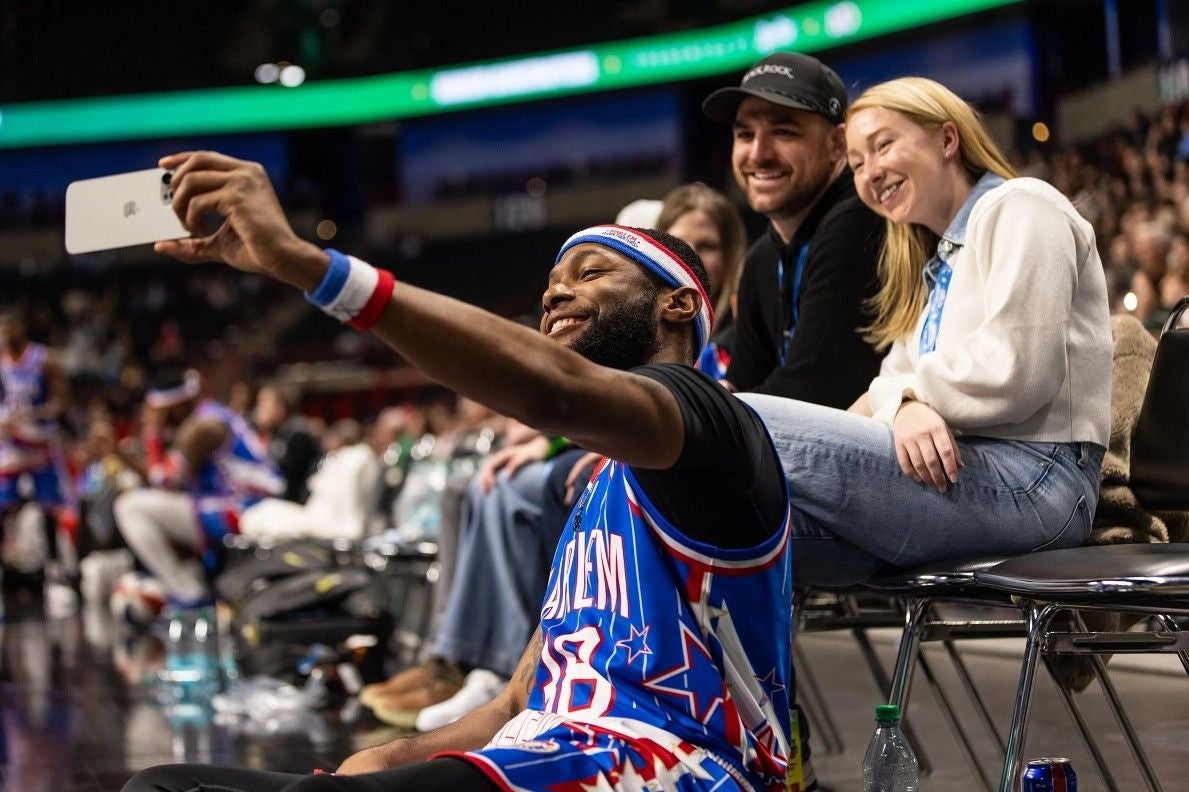 Ein Harlem Globetrotters-Spieler macht ein Selfie mit lachenden Fans am Spielfeldrand.
