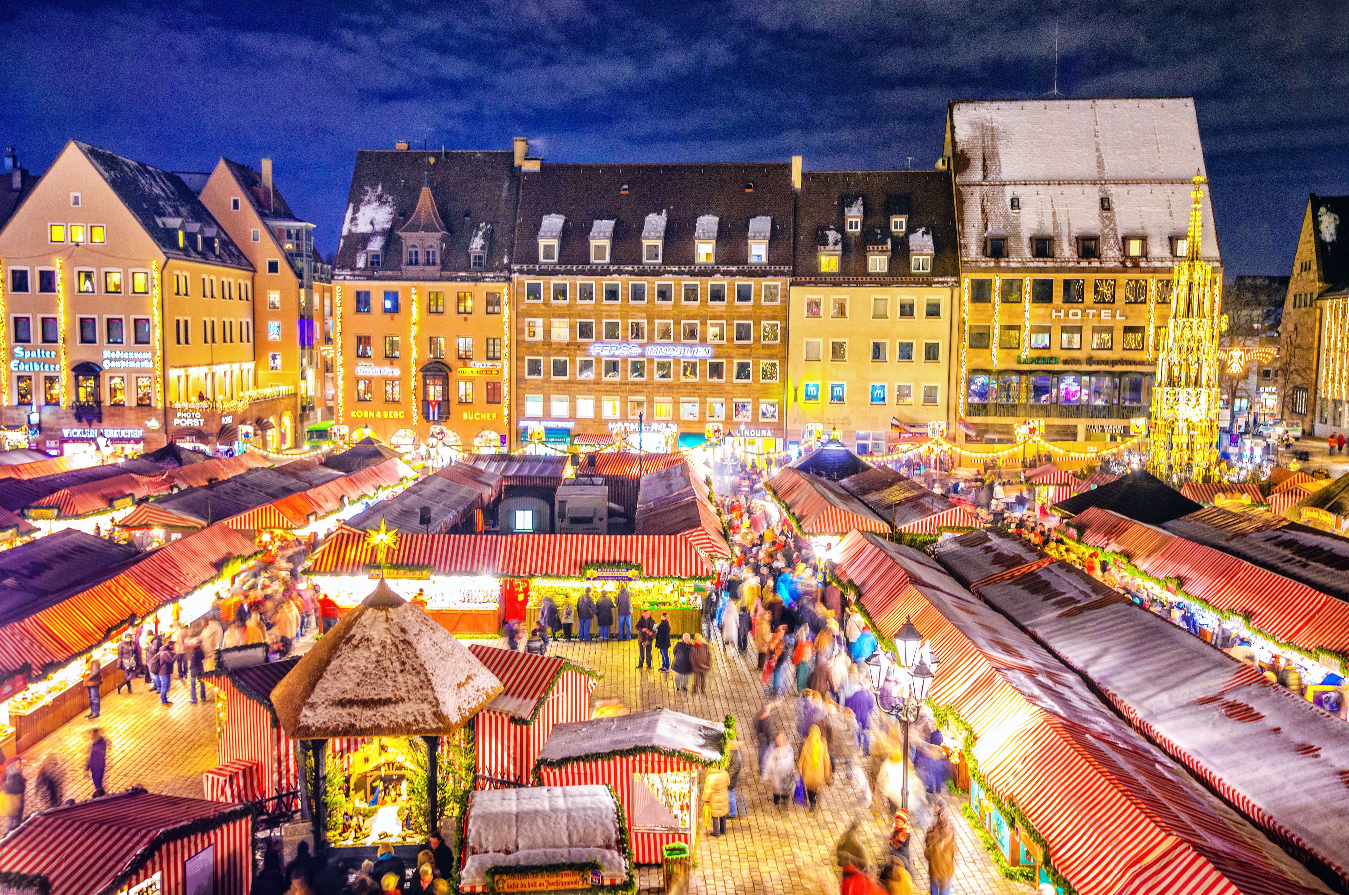 Blick auf den beleuchteten Christkindlesmarkt Nürnberg mit bunten Buden und Besuchern bei Nacht.