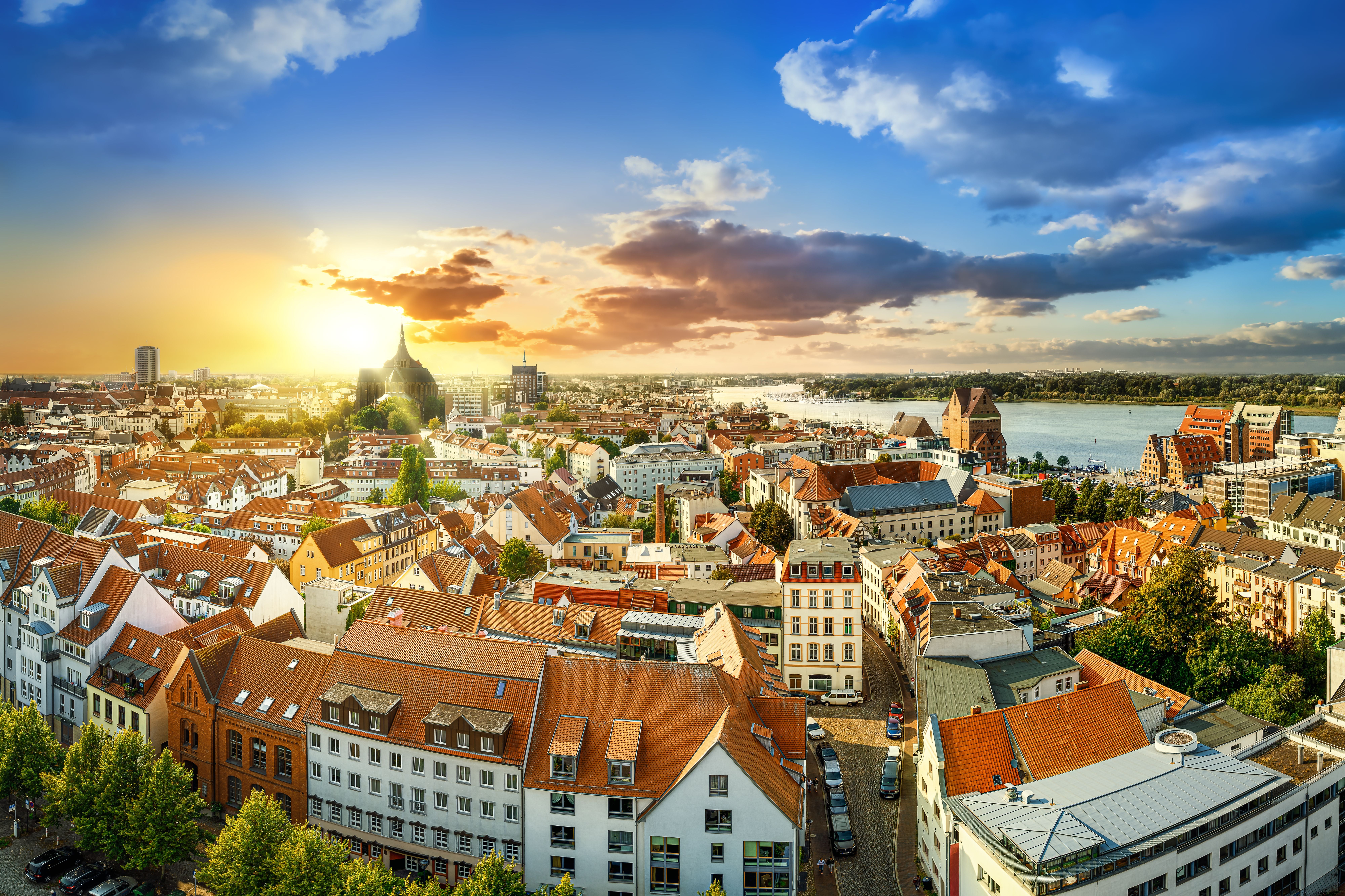 Panoramablick auf das Stadtzentrum von Rostock bei Sonnenuntergang mit roten Dächern und Fluss.