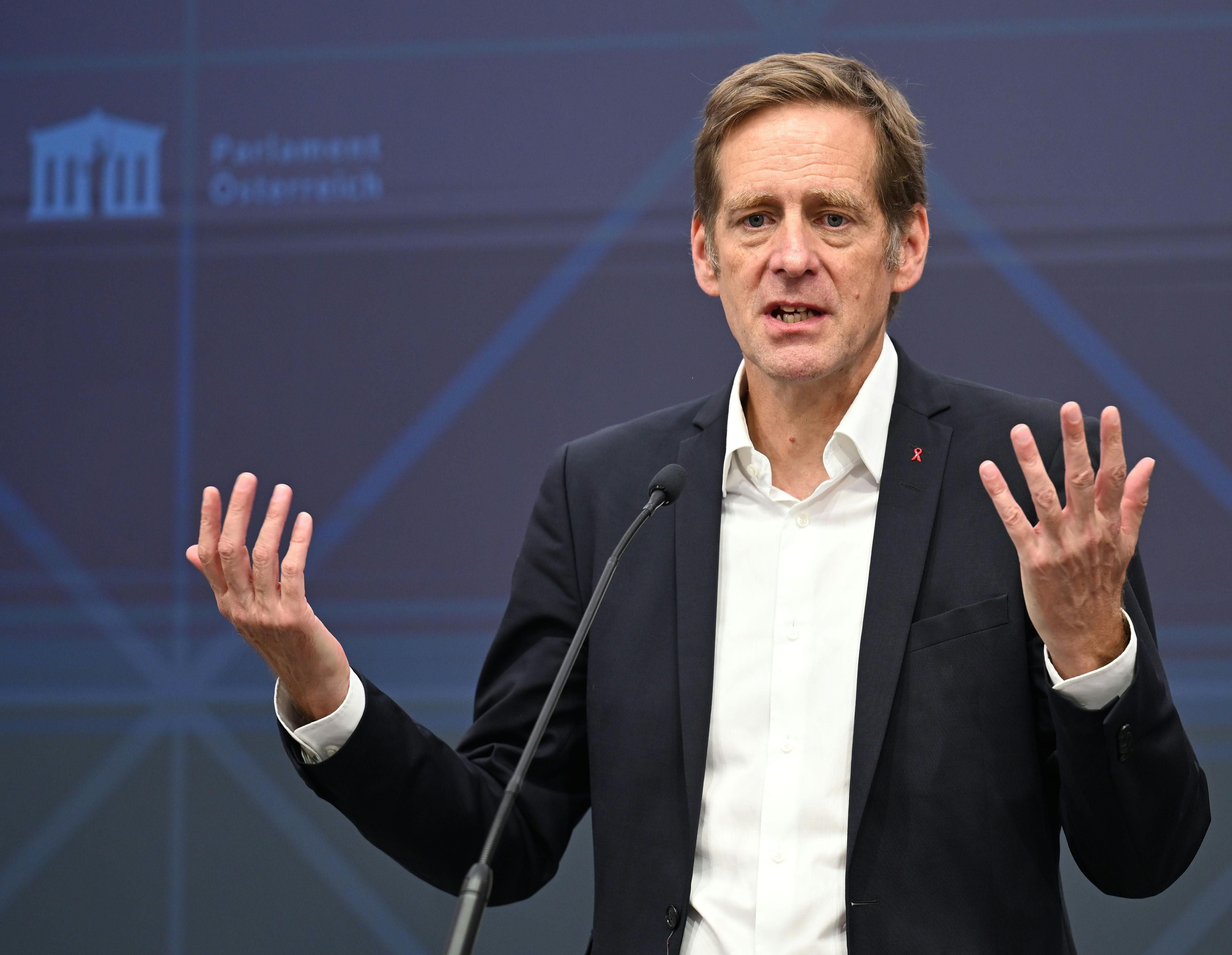 Ein Mann im Anzug spricht gestikulierend am Rednerpult vor dem Logo des österreichischen Parlaments.
