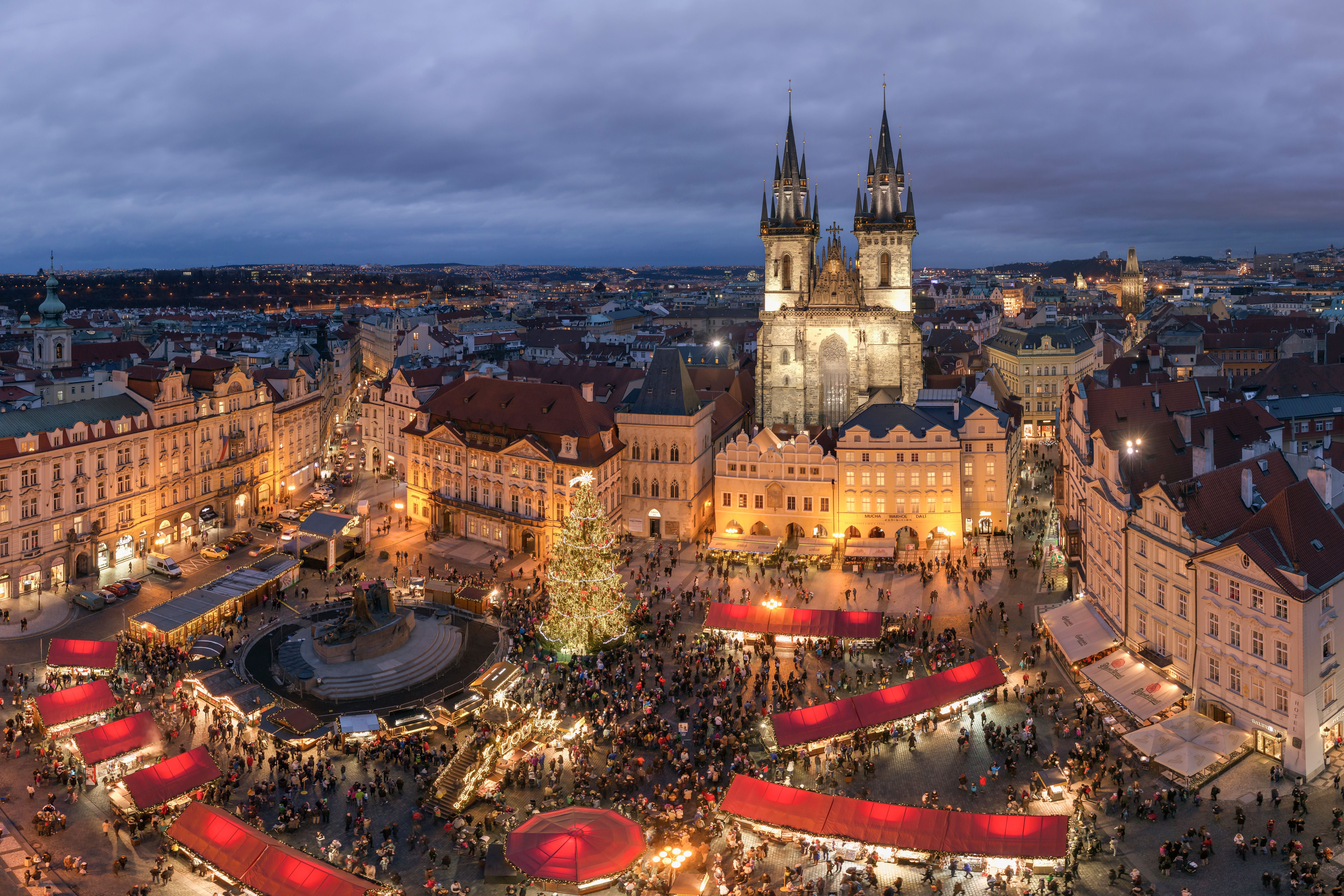 Belebter Weihnachtsmarkt am Abend auf einem historischen Platz mit erleuchtetem Tannenbaum und Kirche.