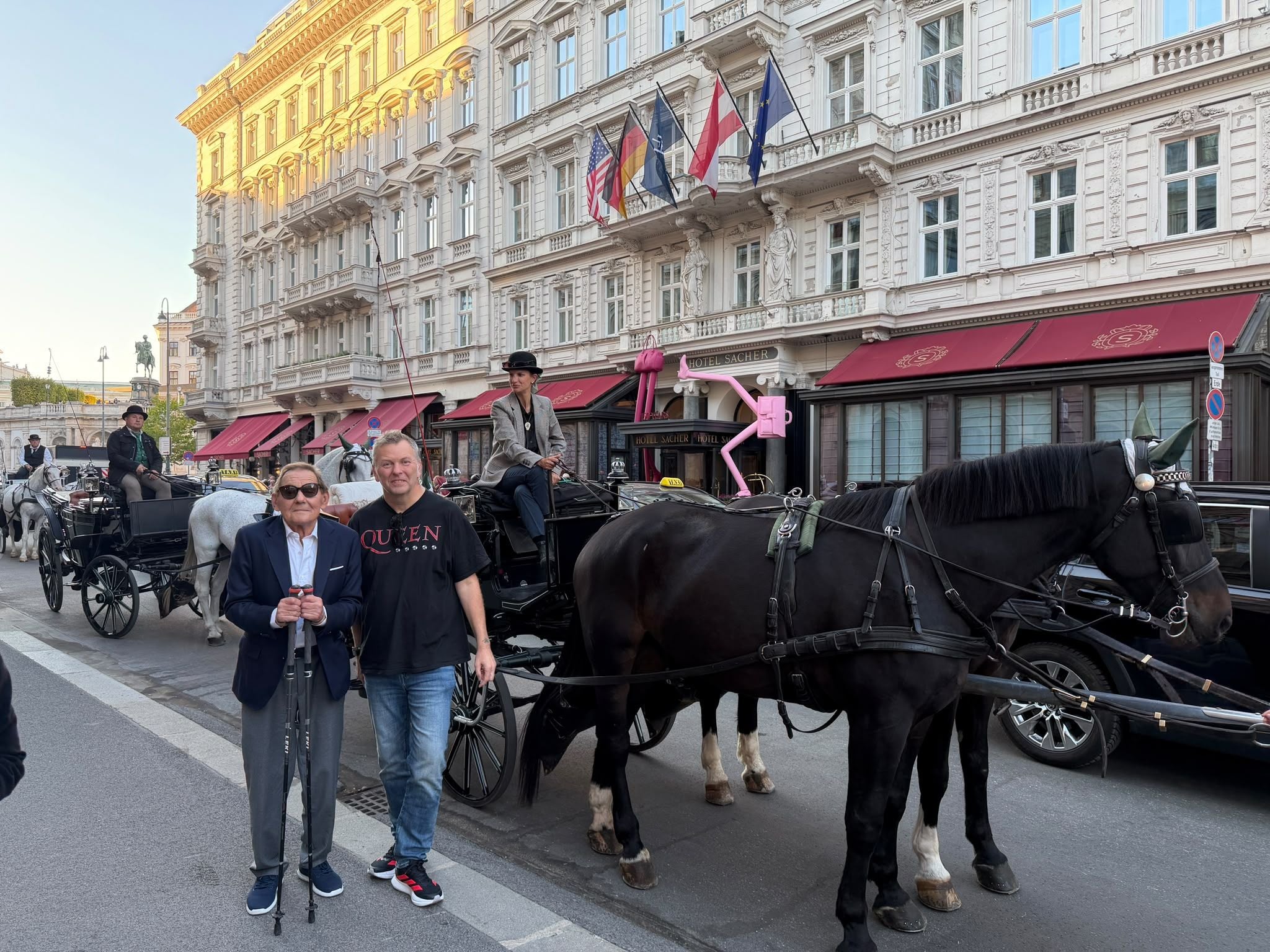 Zwei Männer stehen vor einer Pferdekutsche vor dem Hotel Sacher in Wien.