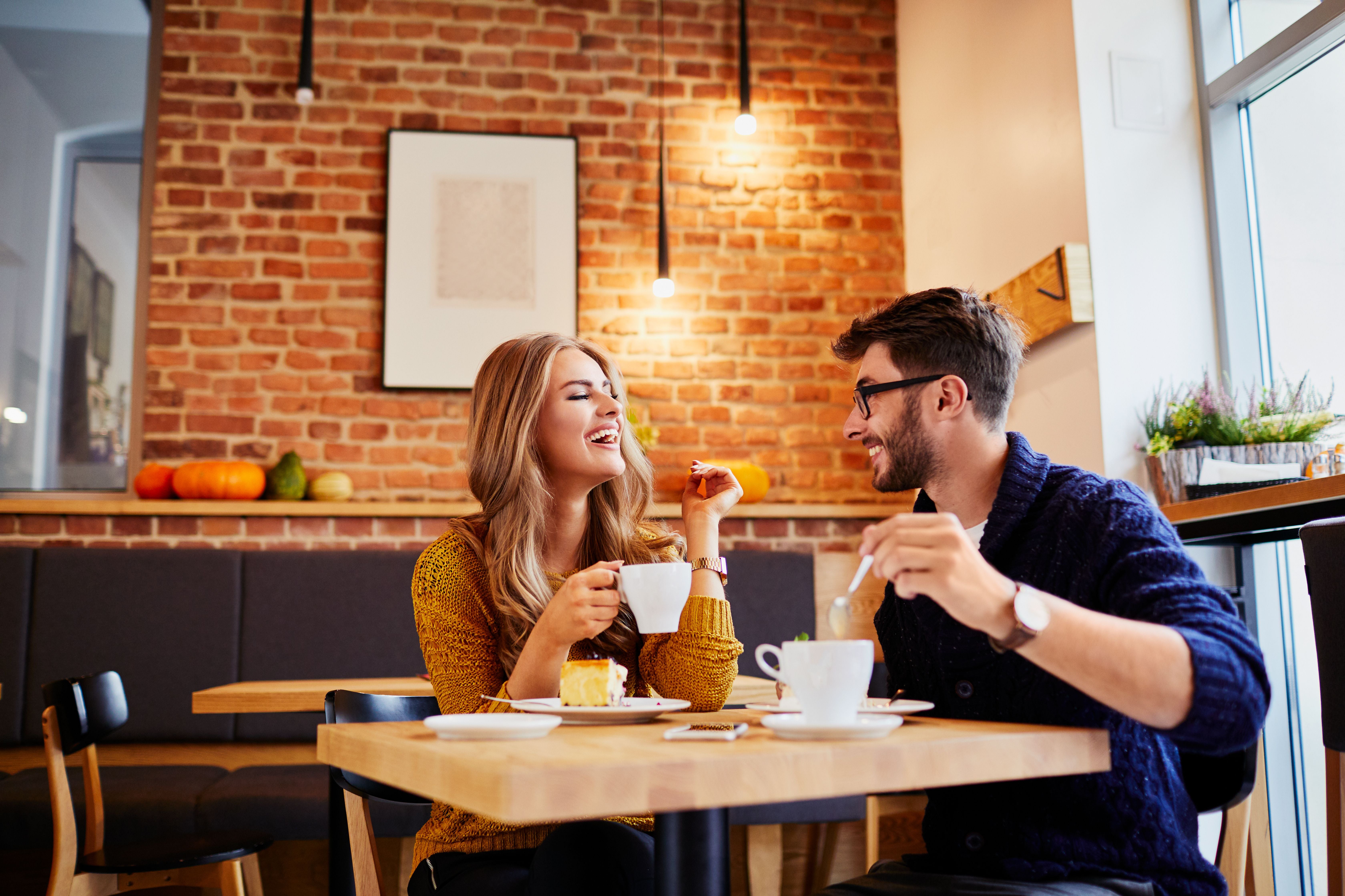 Junges Paar trinkt Kaffee und isst Kuchen in einem modernen Café mit Backsteinwand.