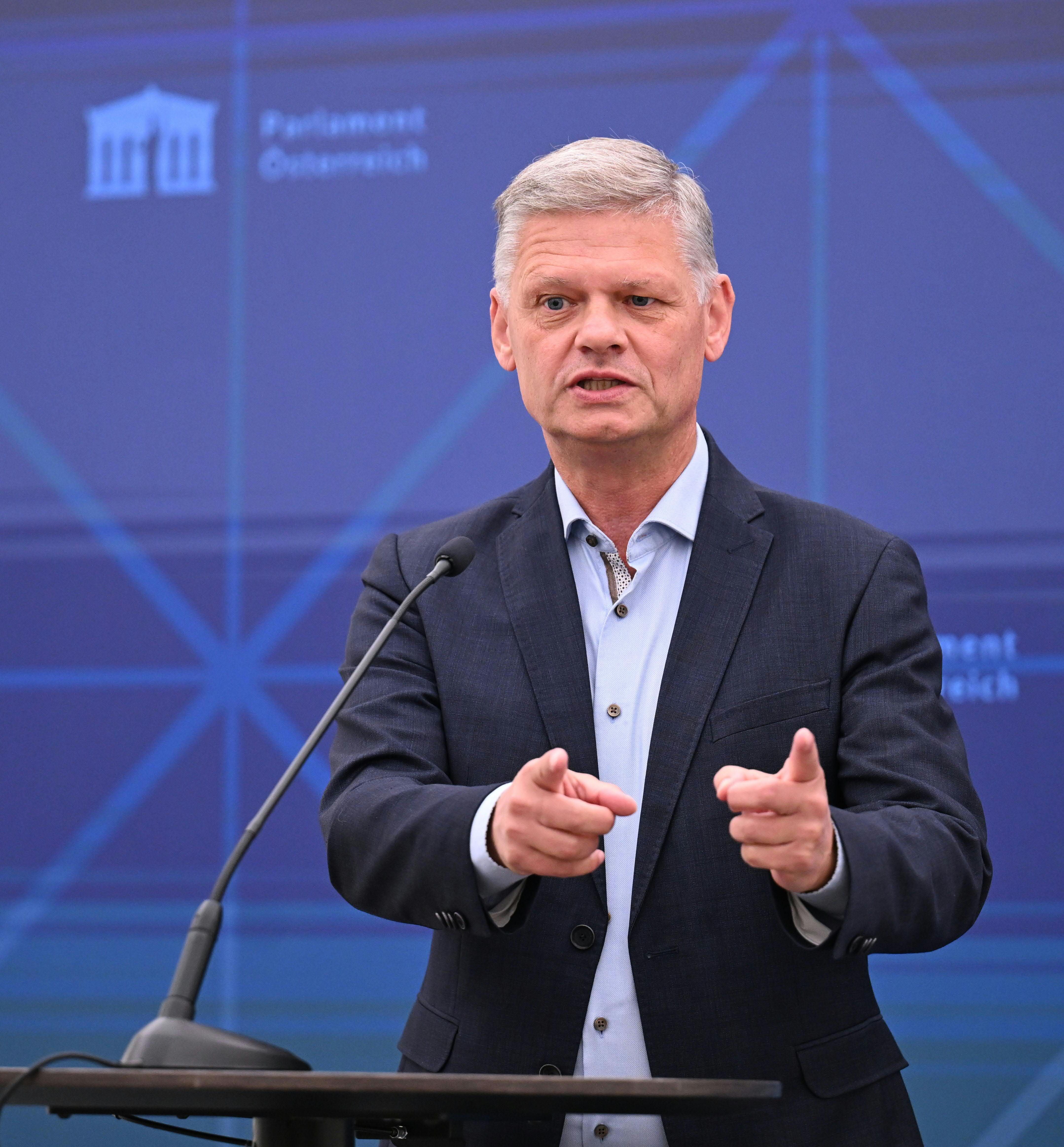 Ein Mann spricht bei einer Pressekonferenz und gestikuliert vor Mikrofonen.