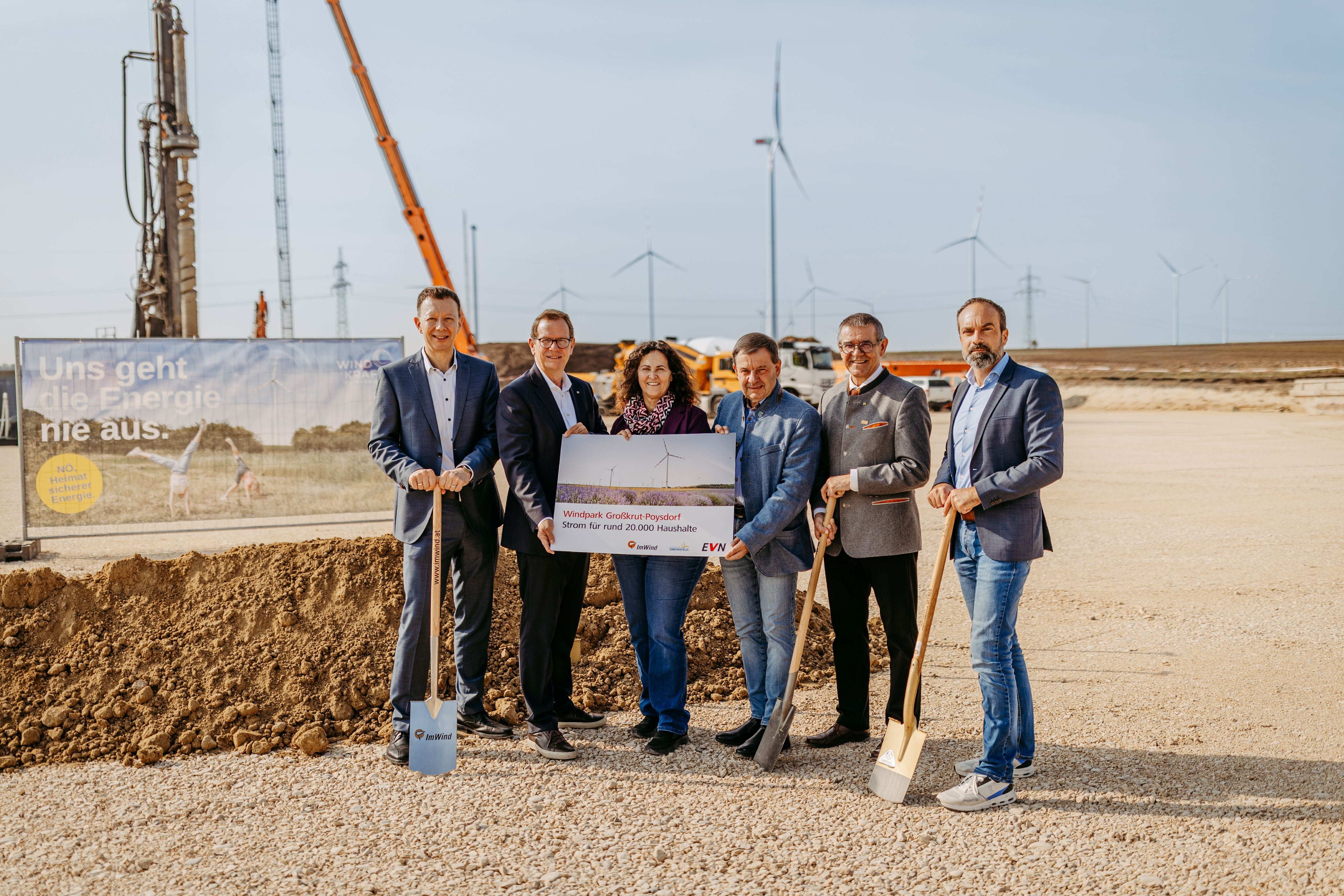 Sechs Personen stehen mit Spaten und einem Schild auf einer Baustelle für einen Windpark.