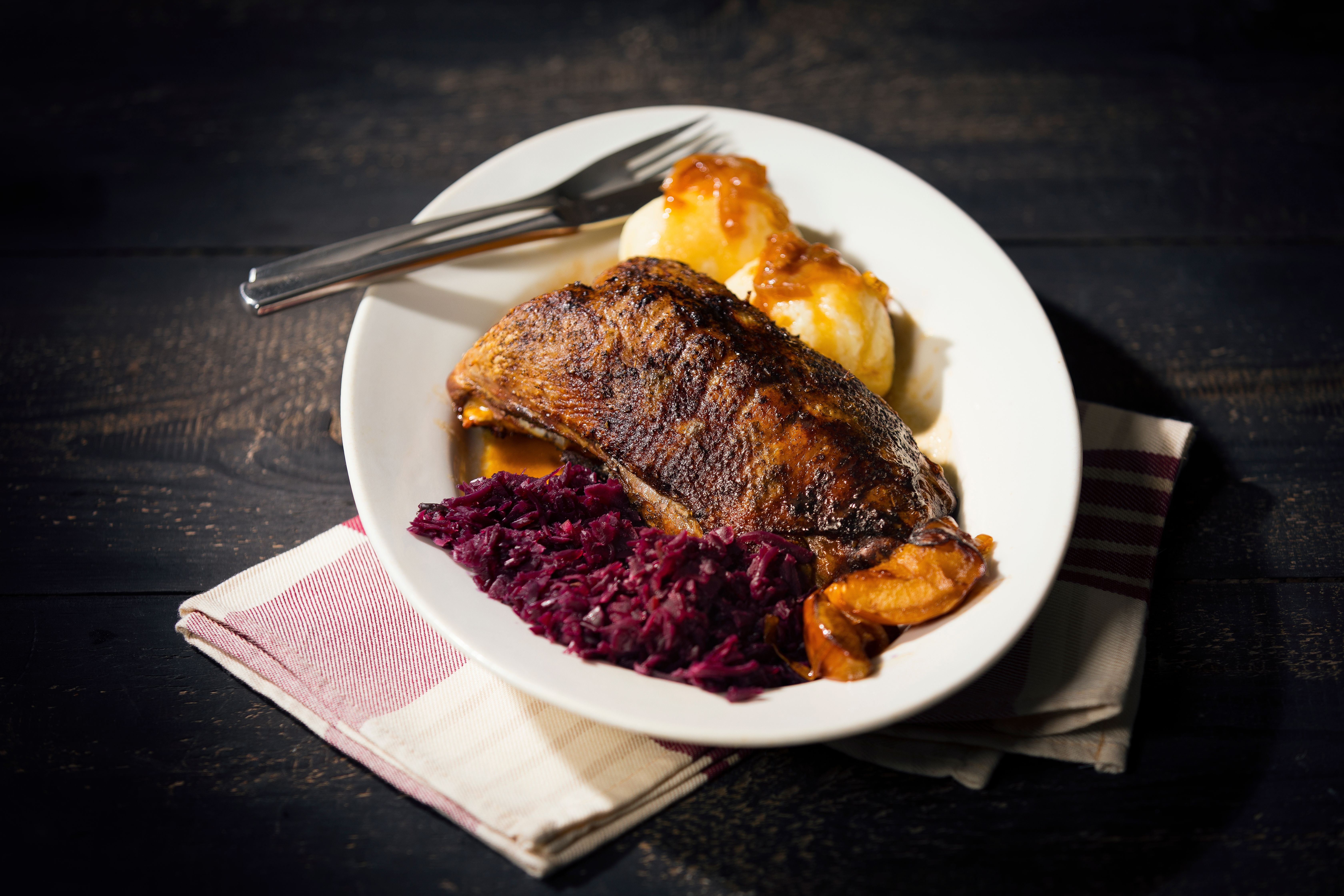 Ein Teller mit gebratener Ente, Rotkohl und zwei Kartoffelklößen mit Soße.