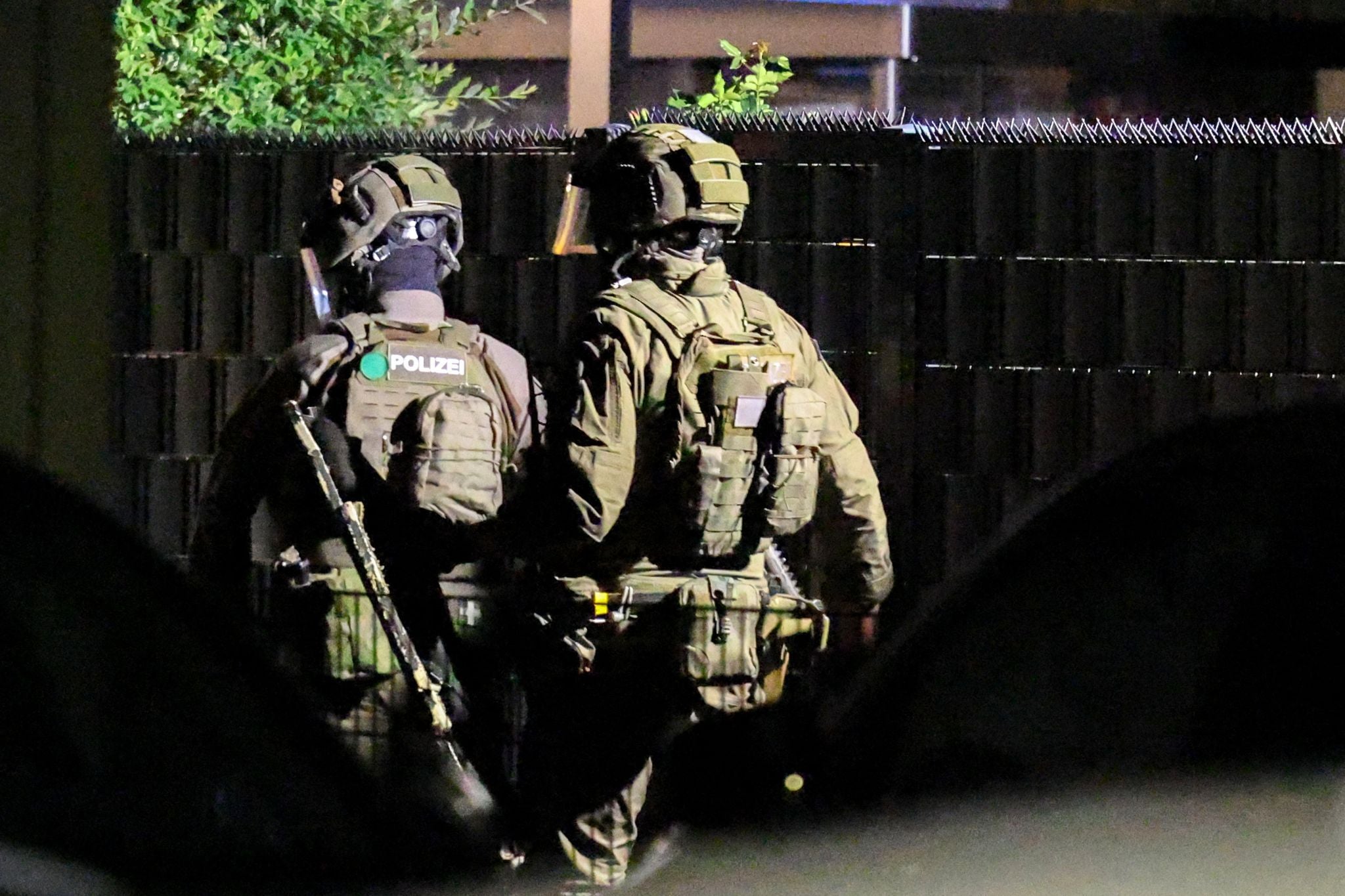 Zwei SEK-Polizisten in voller Ausrüstung stehen nachts vor einem Wohnhaus.
