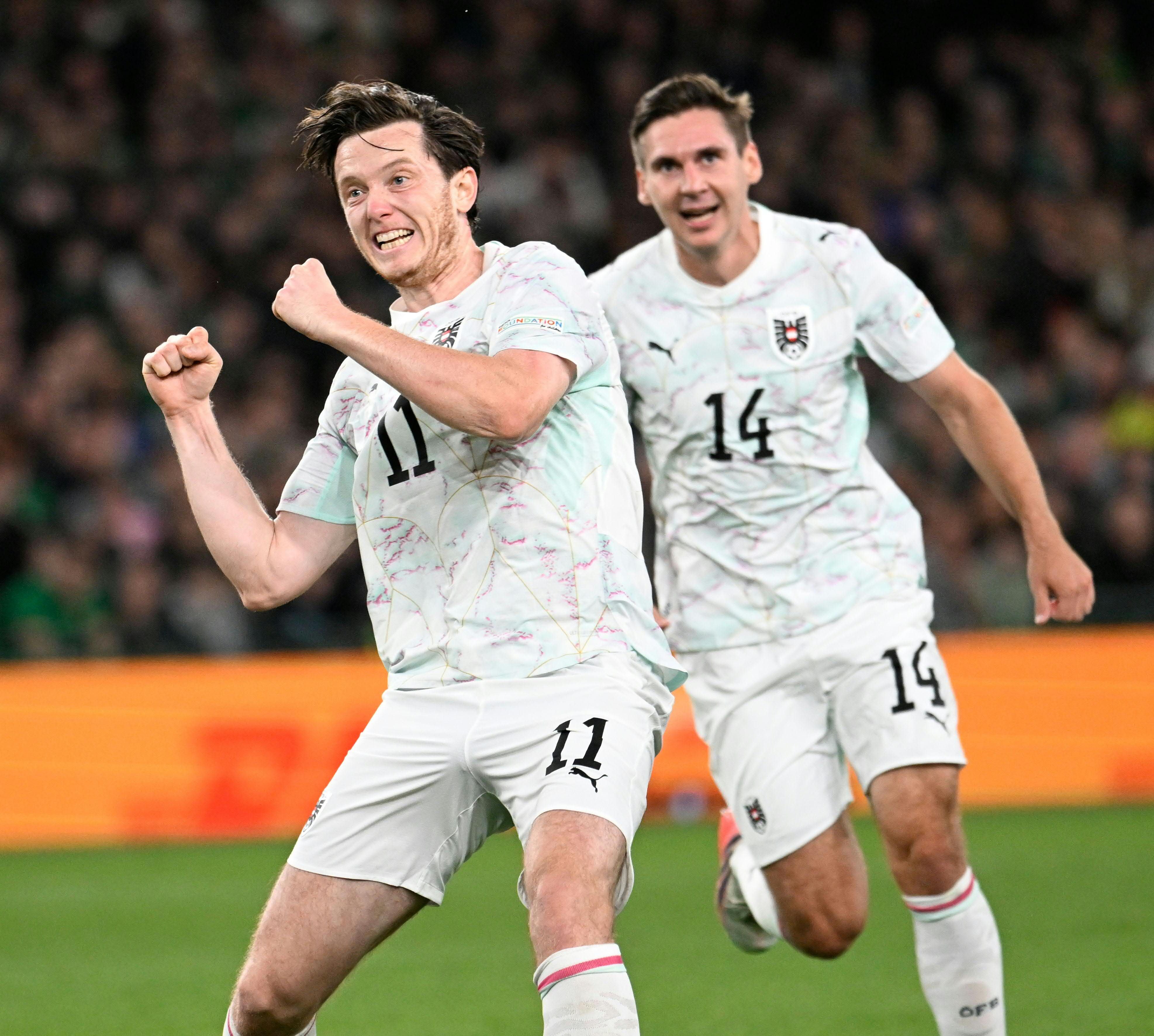 Zwei österreichische Fußballspieler jubeln während eines Spiels gegen Irland auf dem Spielfeld.