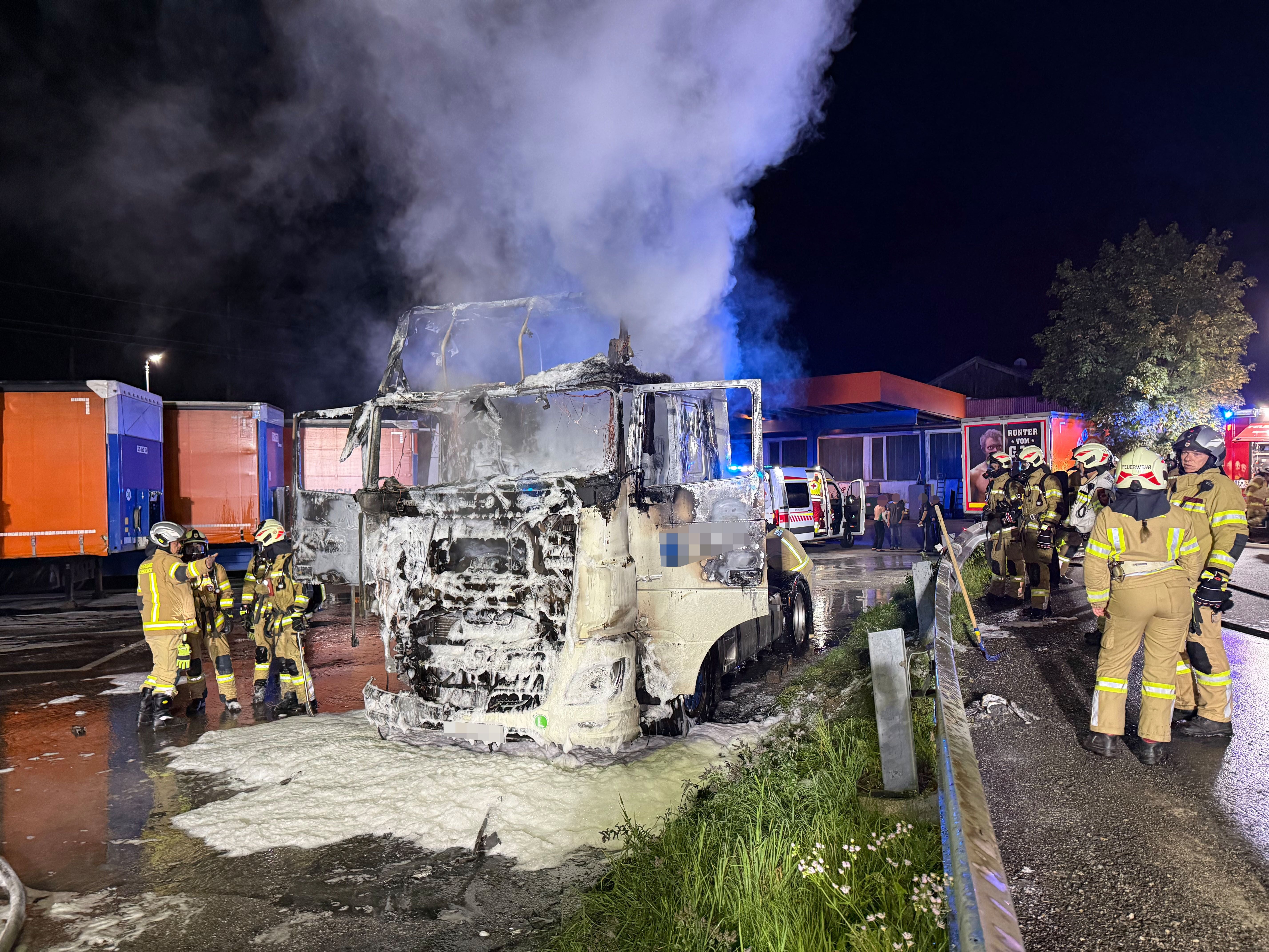 Feuerwehrleute löschen nachts einen brennenden LKW, aus dem dichter Rauch aufsteigt.