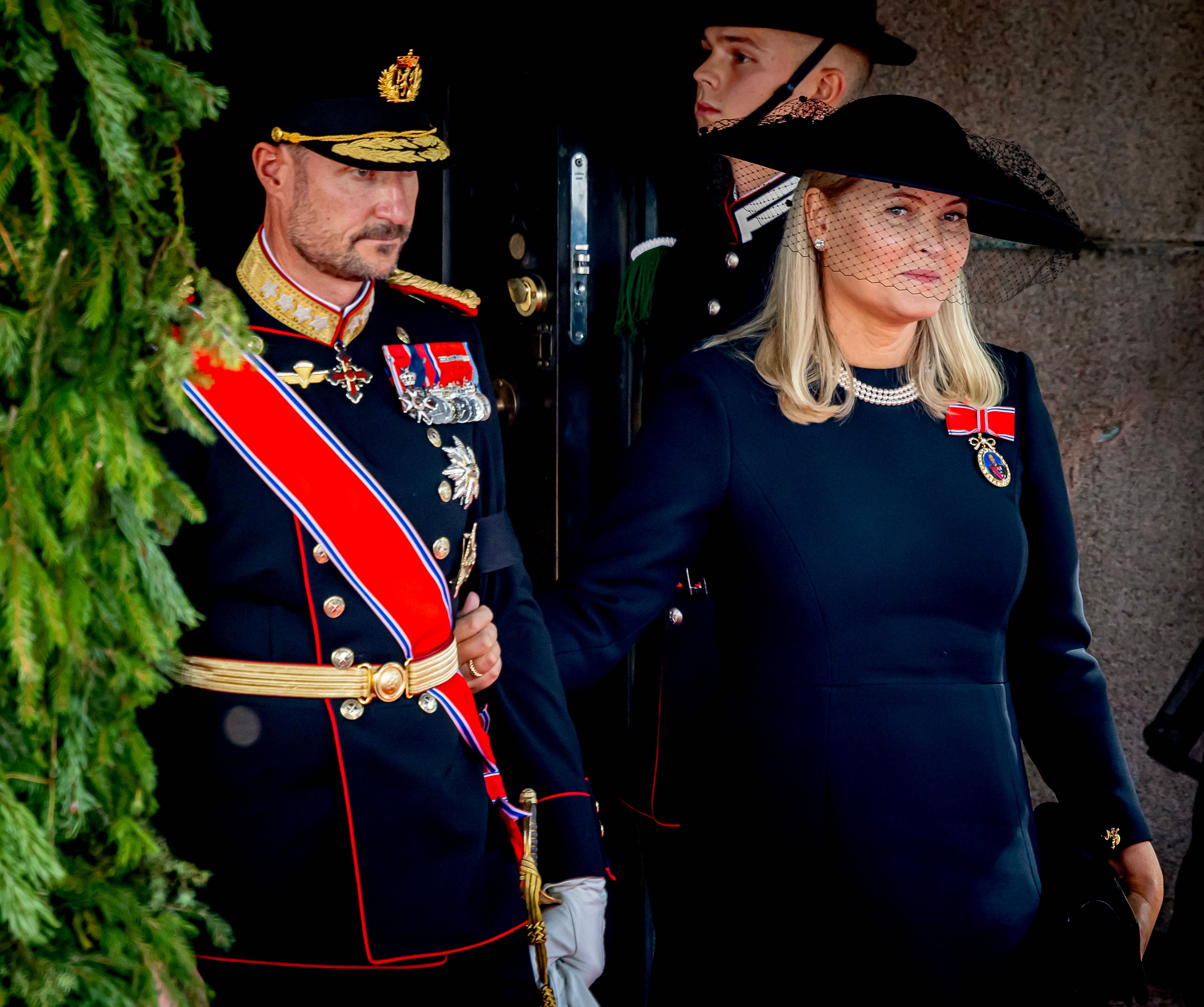 König und Königin in eleganter Trauerkleidung bei einer royalen Prozession in Oslo.