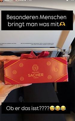 Hand hält eine rote Schachtel Original Sacher Torte im Flugzeug, mit Text im Bild.