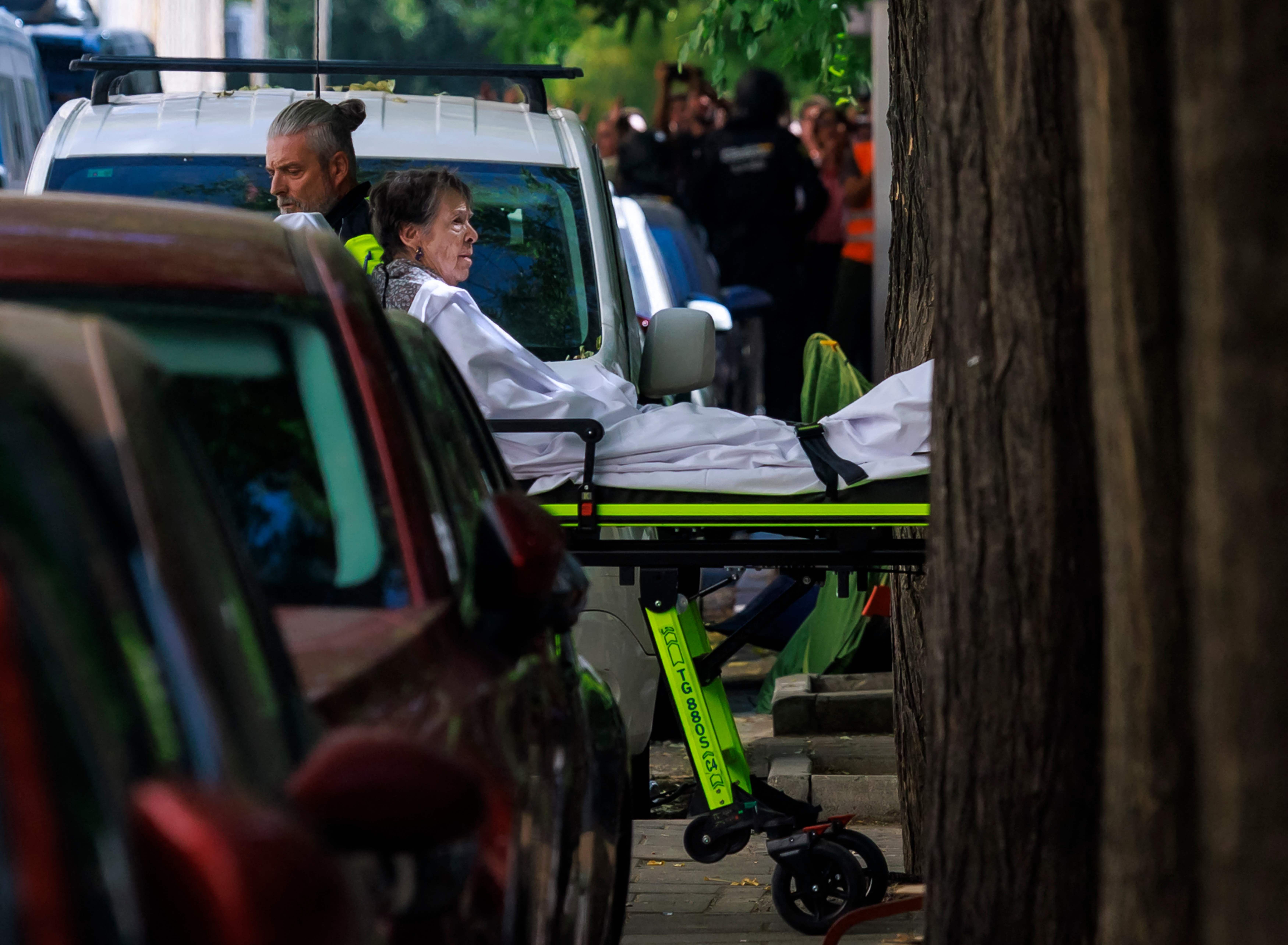 Eine ältere Frau wird auf einer Trage von einem Sanitäter auf einer Straße transportiert.