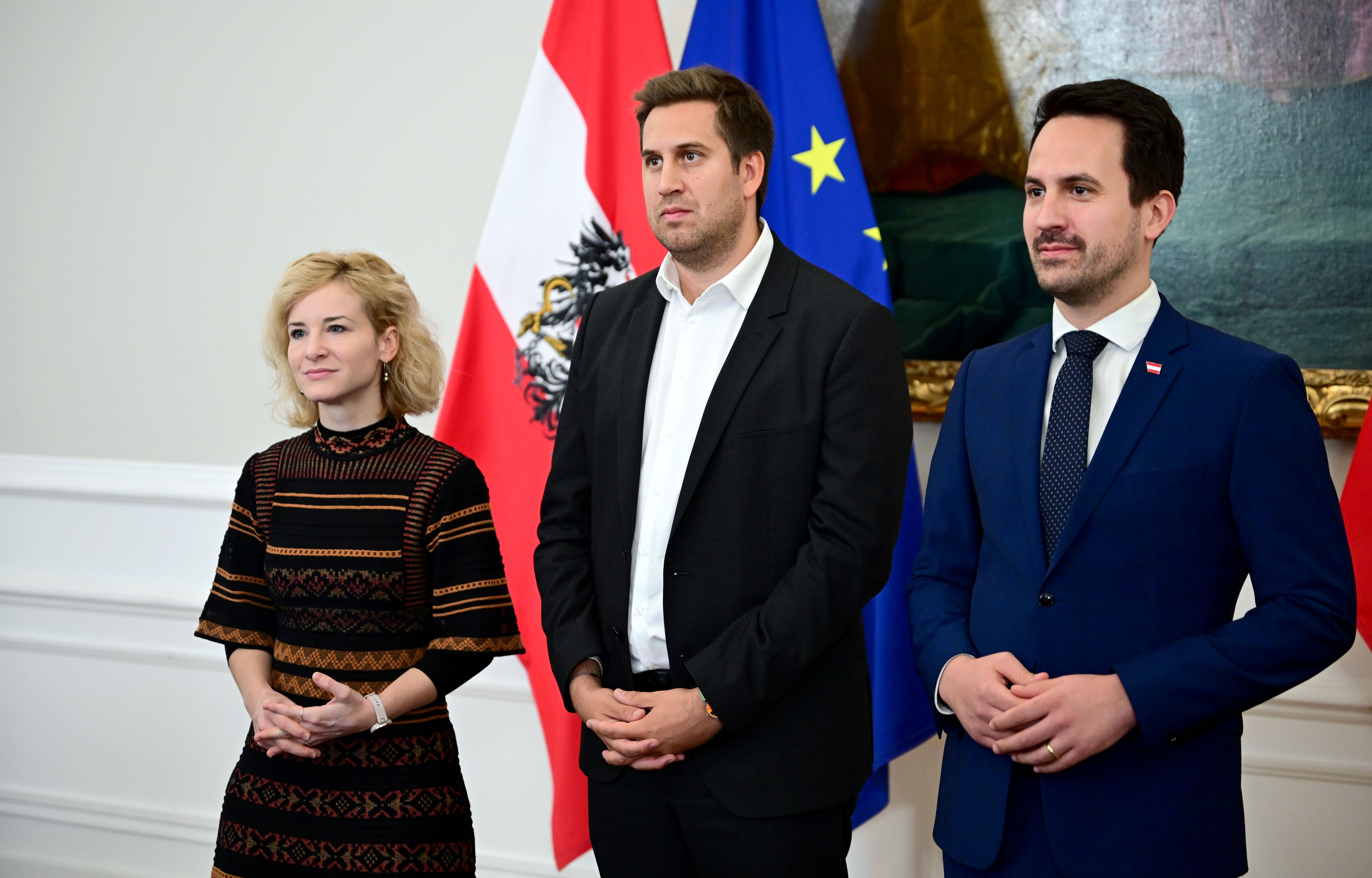 Drei Personen stehen nebeneinander vor österreichischer und EU-Flagge bei einem Pressetermin.