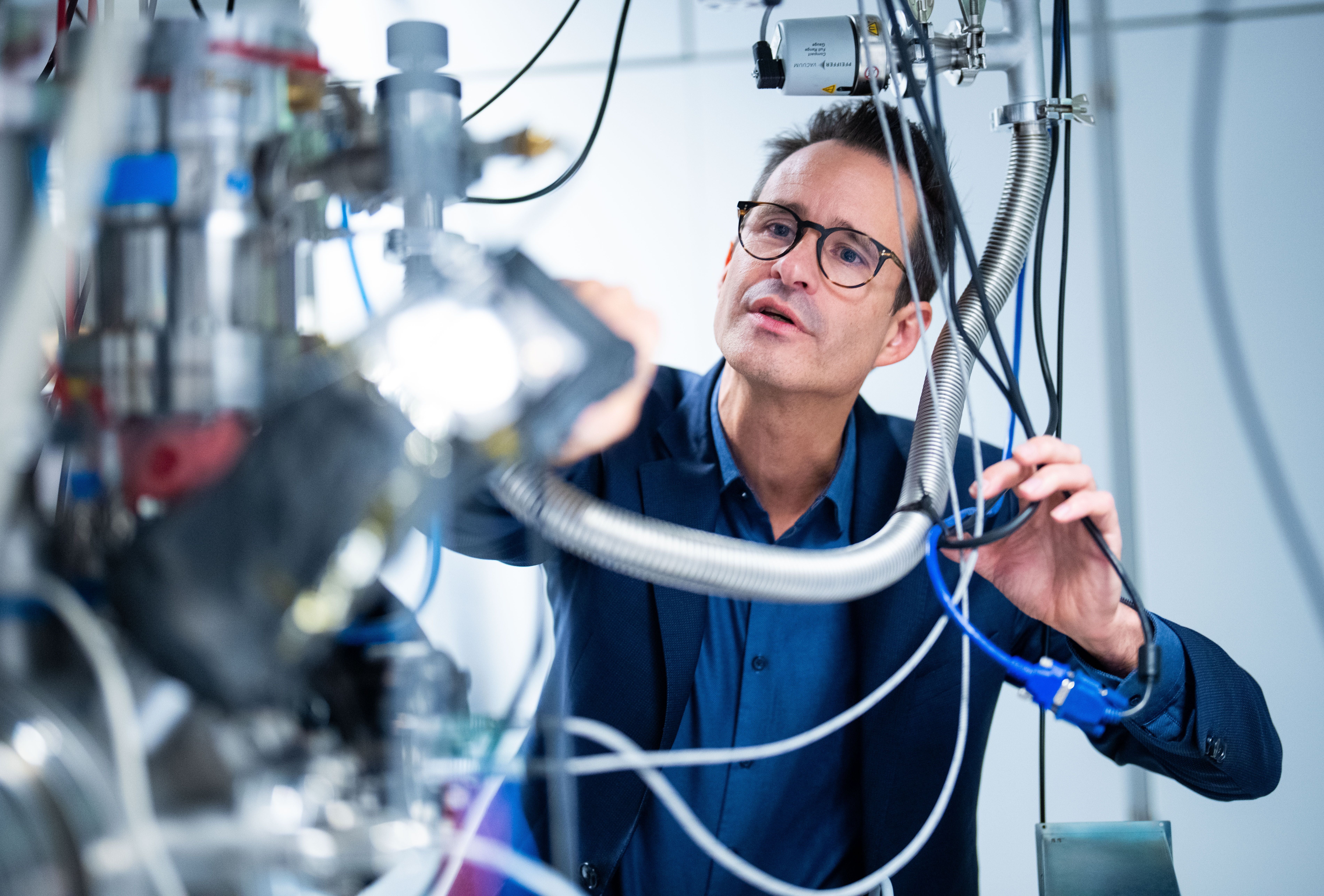 Ein Mann arbeitet an einer komplexen wissenschaftlichen Apparatur mit vielen Kabeln und Metallteilen.