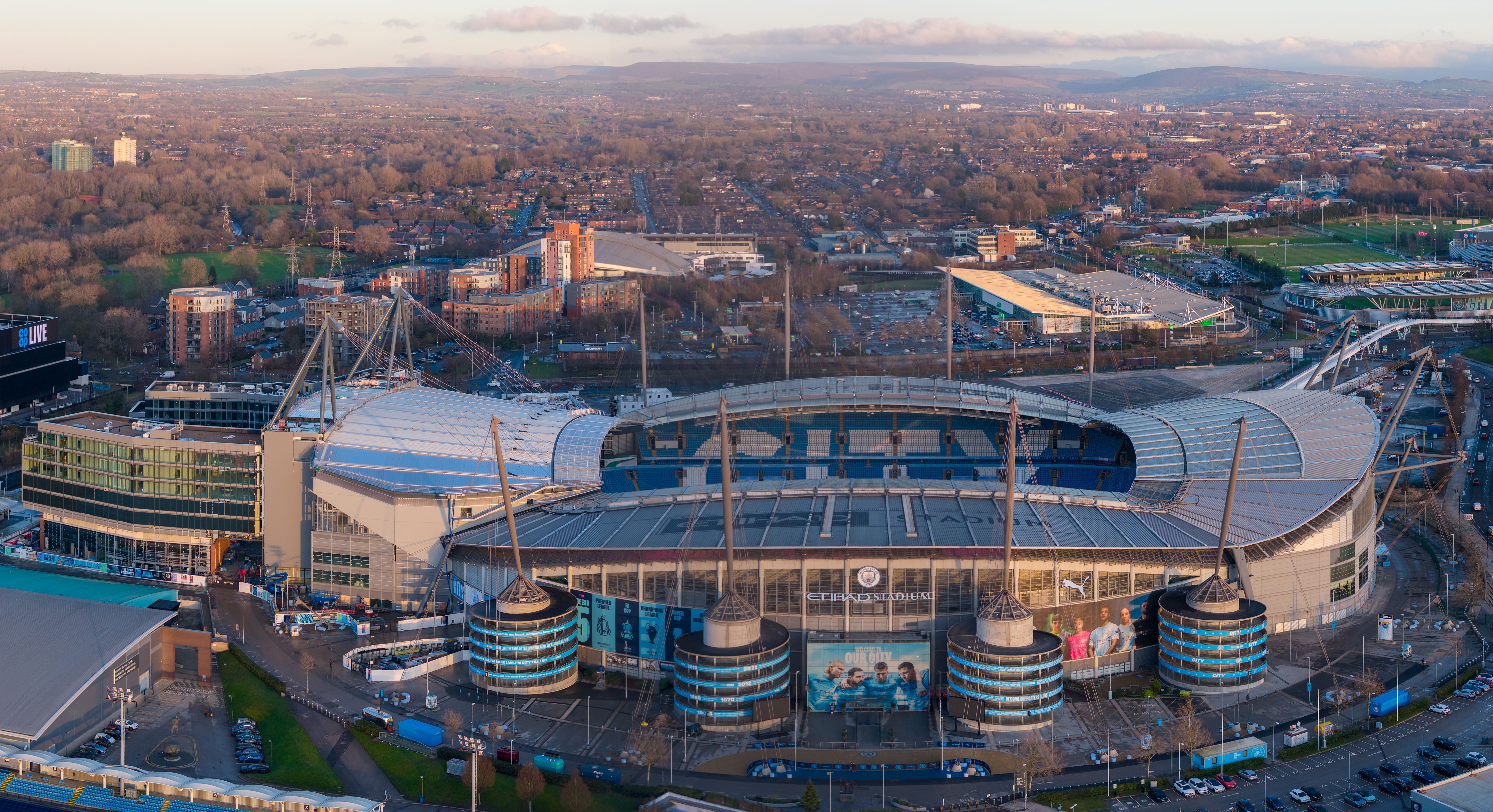 Luftaufnahme des Etihad Campus mit Manchester City Stadion und Joie Stadium bei Sonnenuntergang.