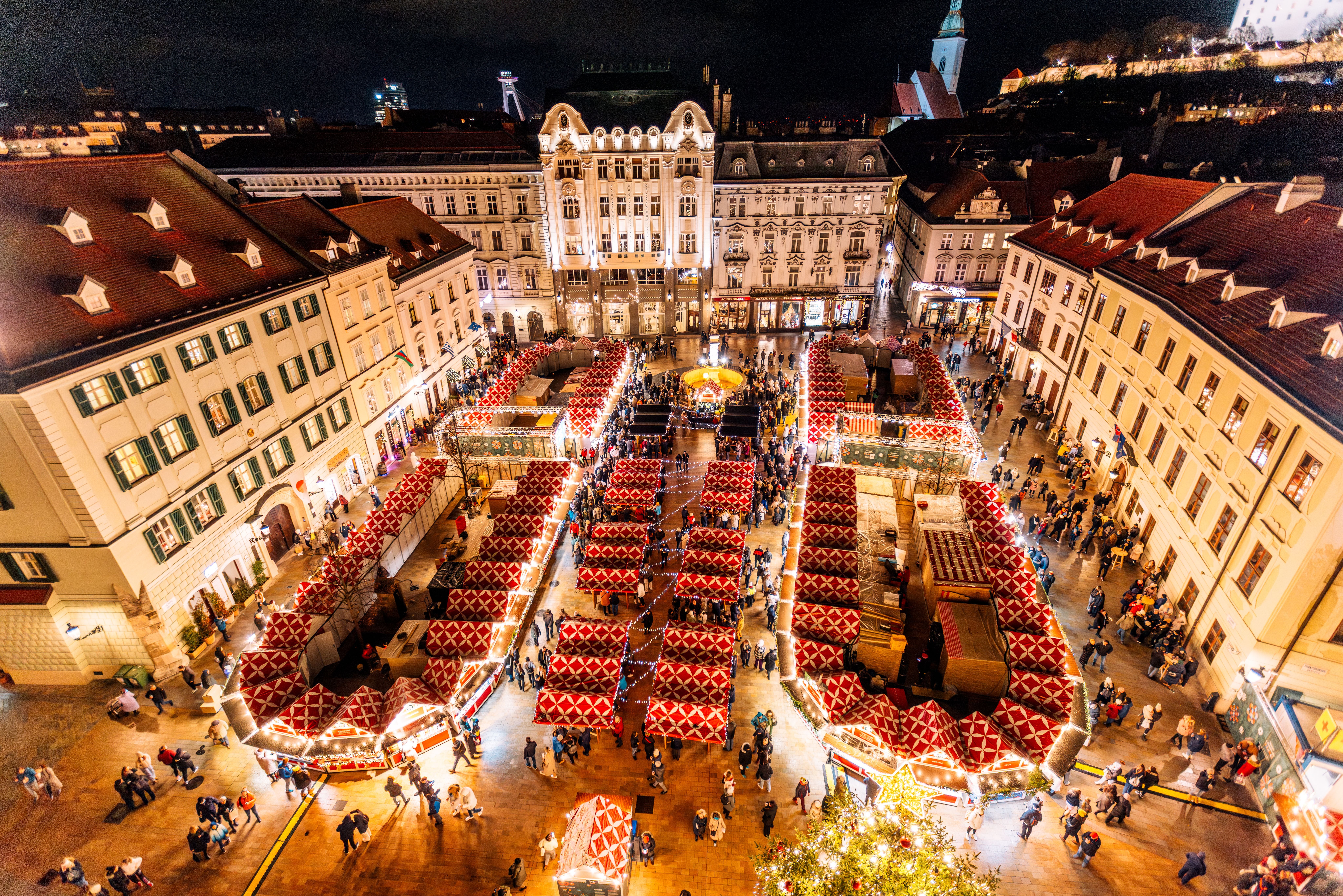 Blick auf einen festlich beleuchteten Weihnachtsmarkt mit roten Buden auf einem historischen Platz.