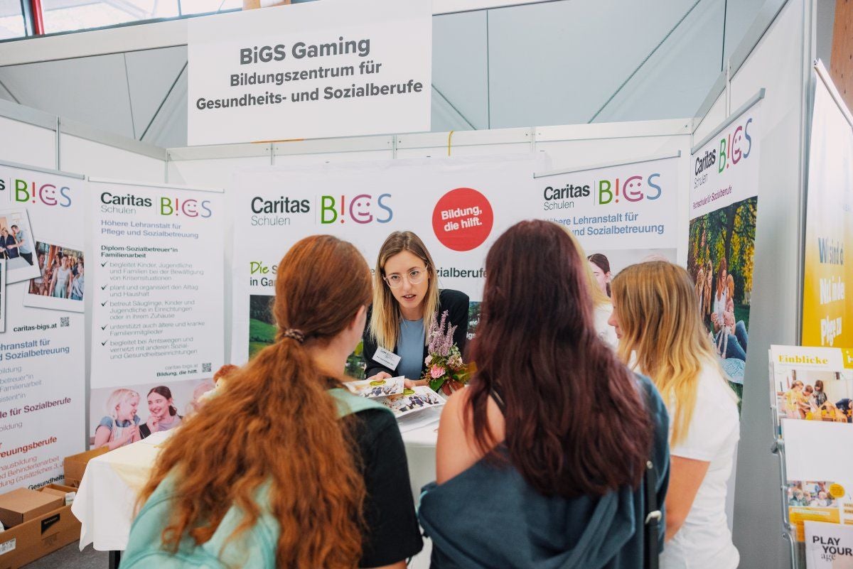Eine Frau informiert drei junge Frauen an einem Messestand des BiGS Bildungszentrums für Sozialberufe.