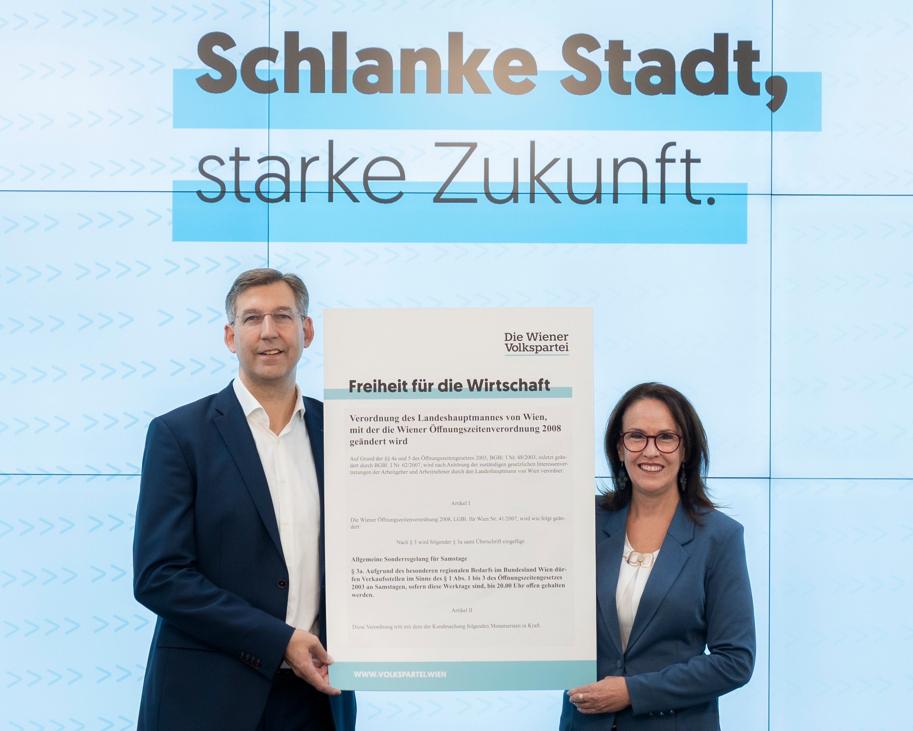 Zwei Personen im Anzug halten ein großes Plakat vor einem Banner mit dem Text „Schlanke Stadt, starke Zukunft.“