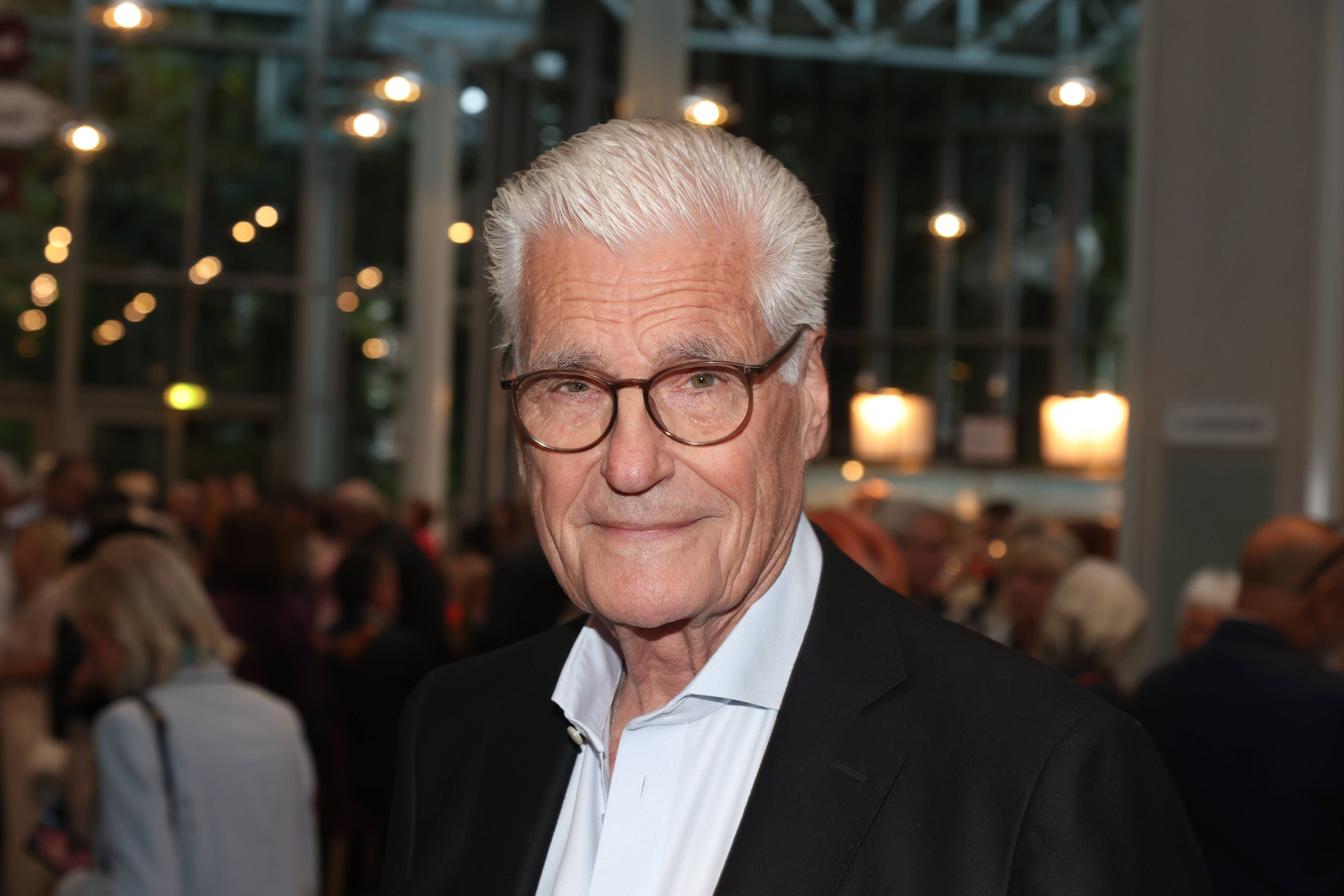 Älterer Mann mit Brille auf einer Premierenfeier in einem belebten Theaterfoyer.