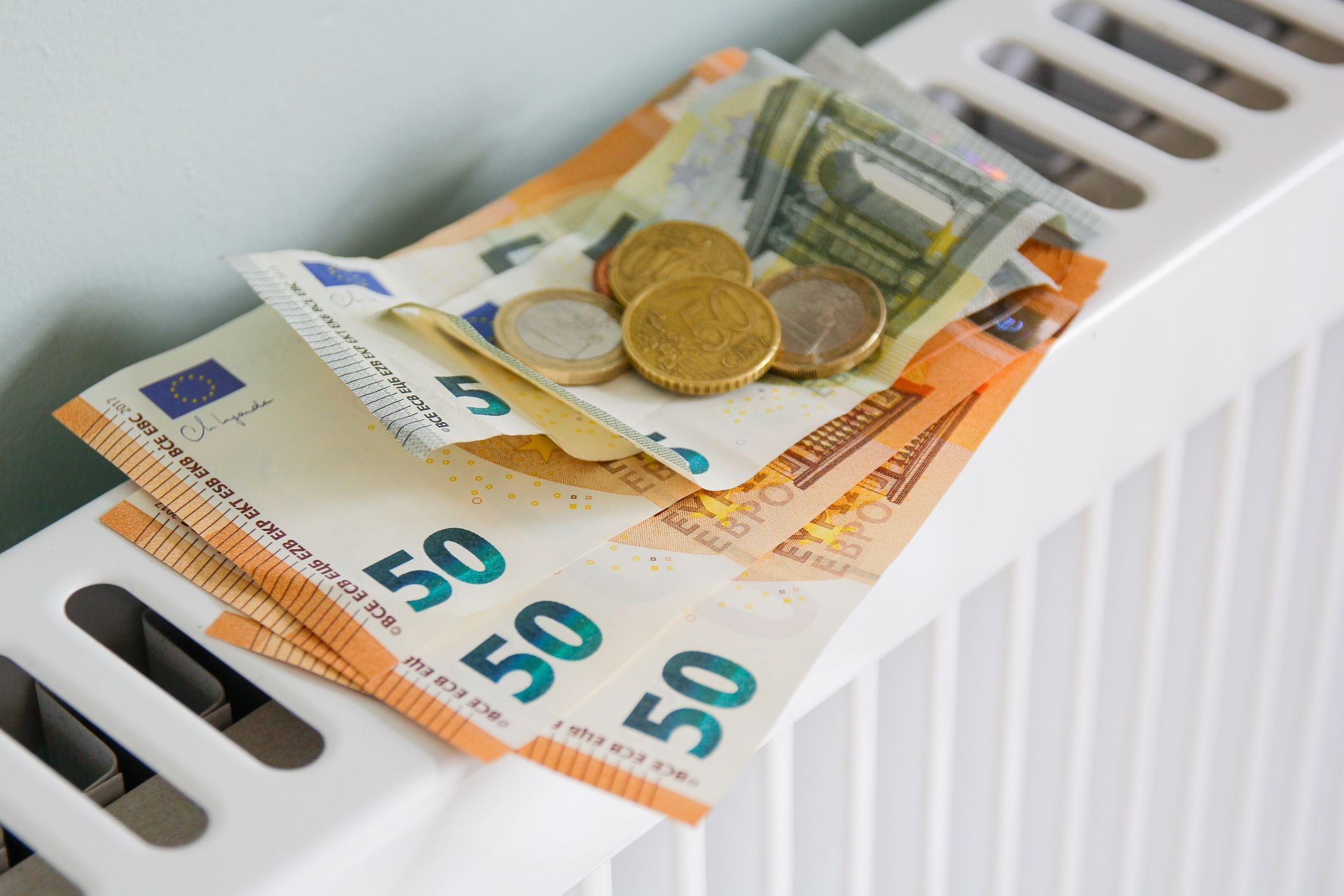 Mehrere Euro-Scheine und Münzen liegen auf einem weißen Heizkörper.