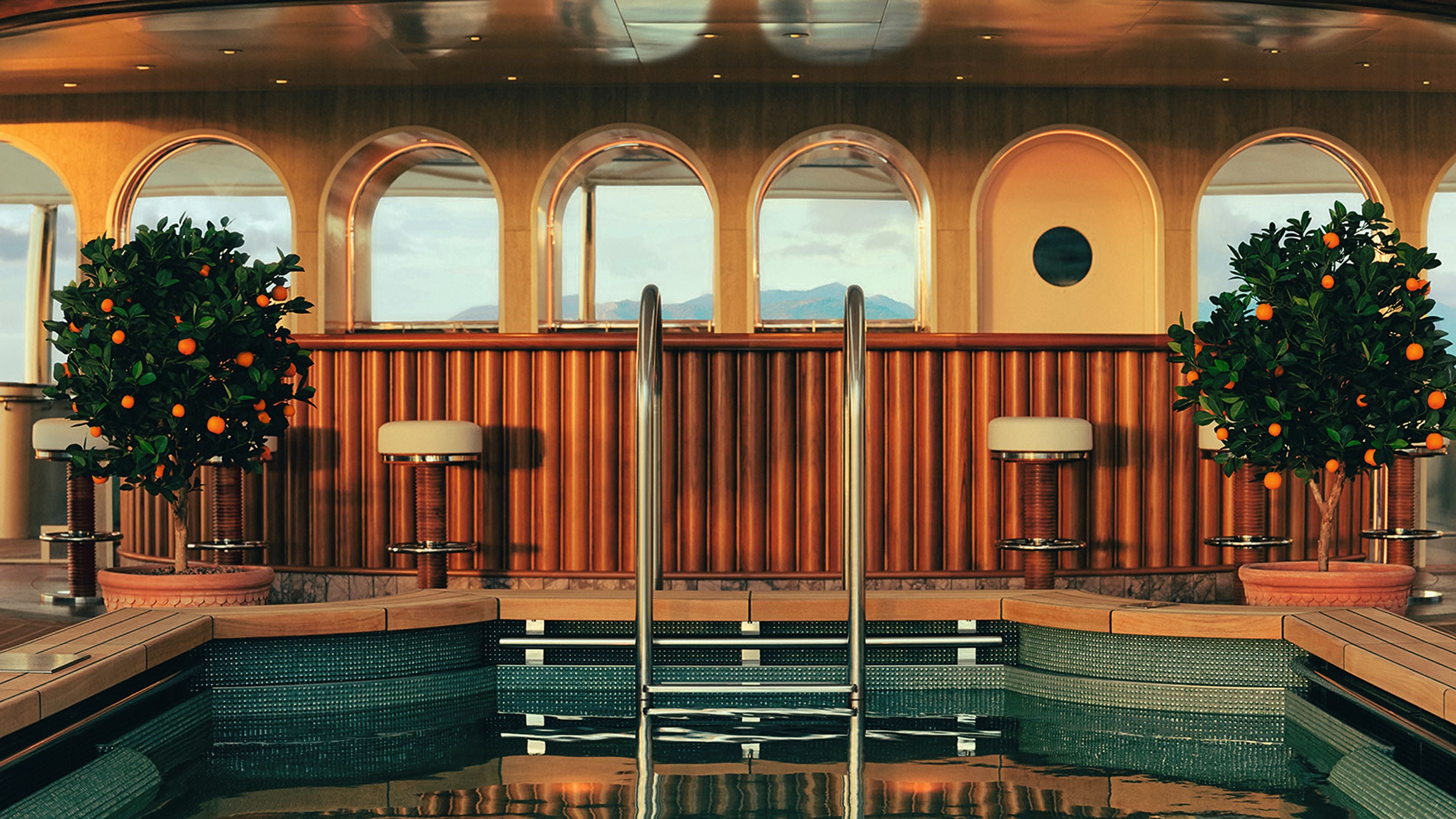 Luxuriöser Poolbereich auf einem Schiff mit Bar, Hockern und zwei Orangenbäumen in Töpfen.