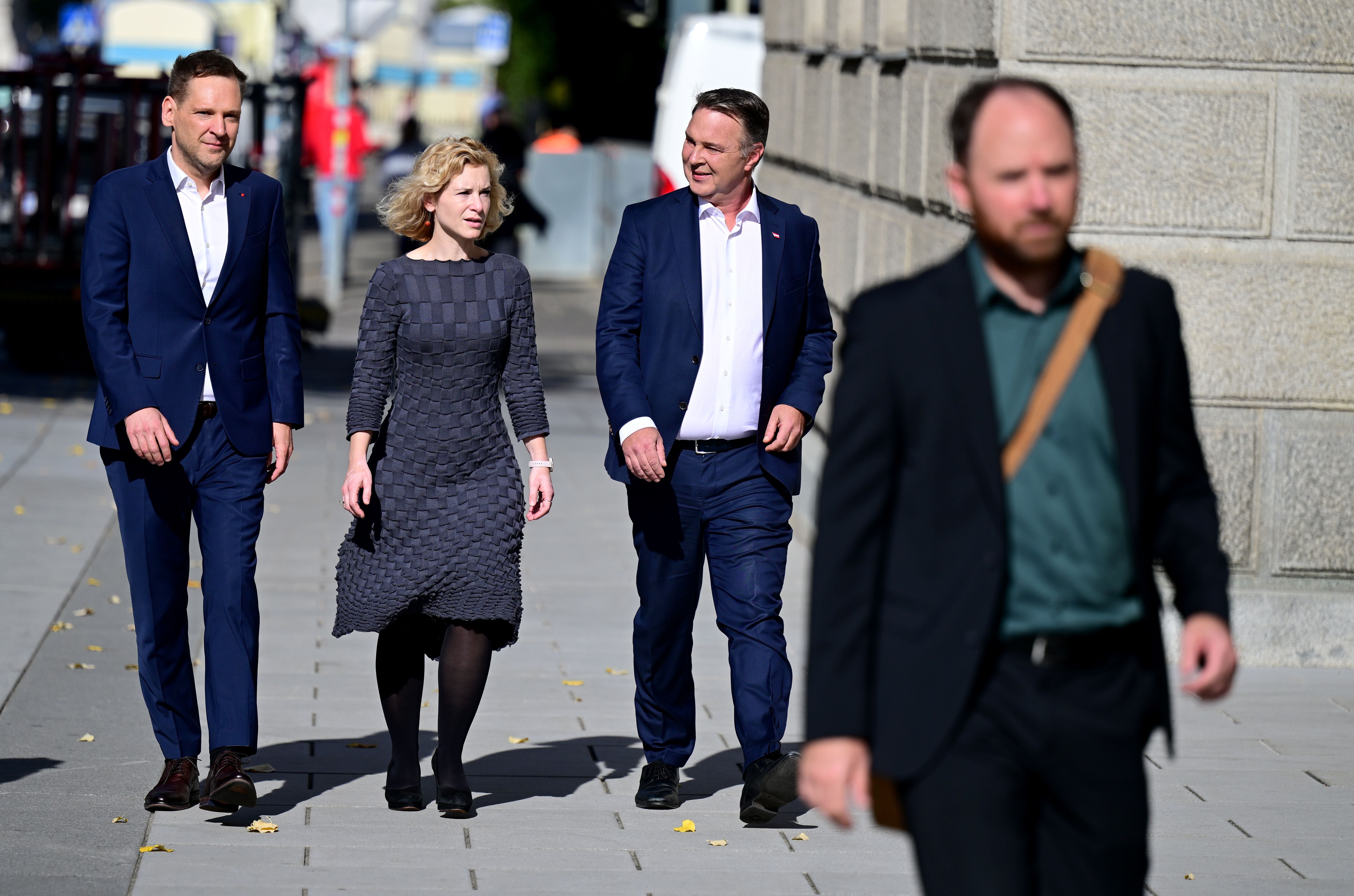 Vier Personen in Businesskleidung gehen auf einem Gehweg neben einem Gebäude in Wien.