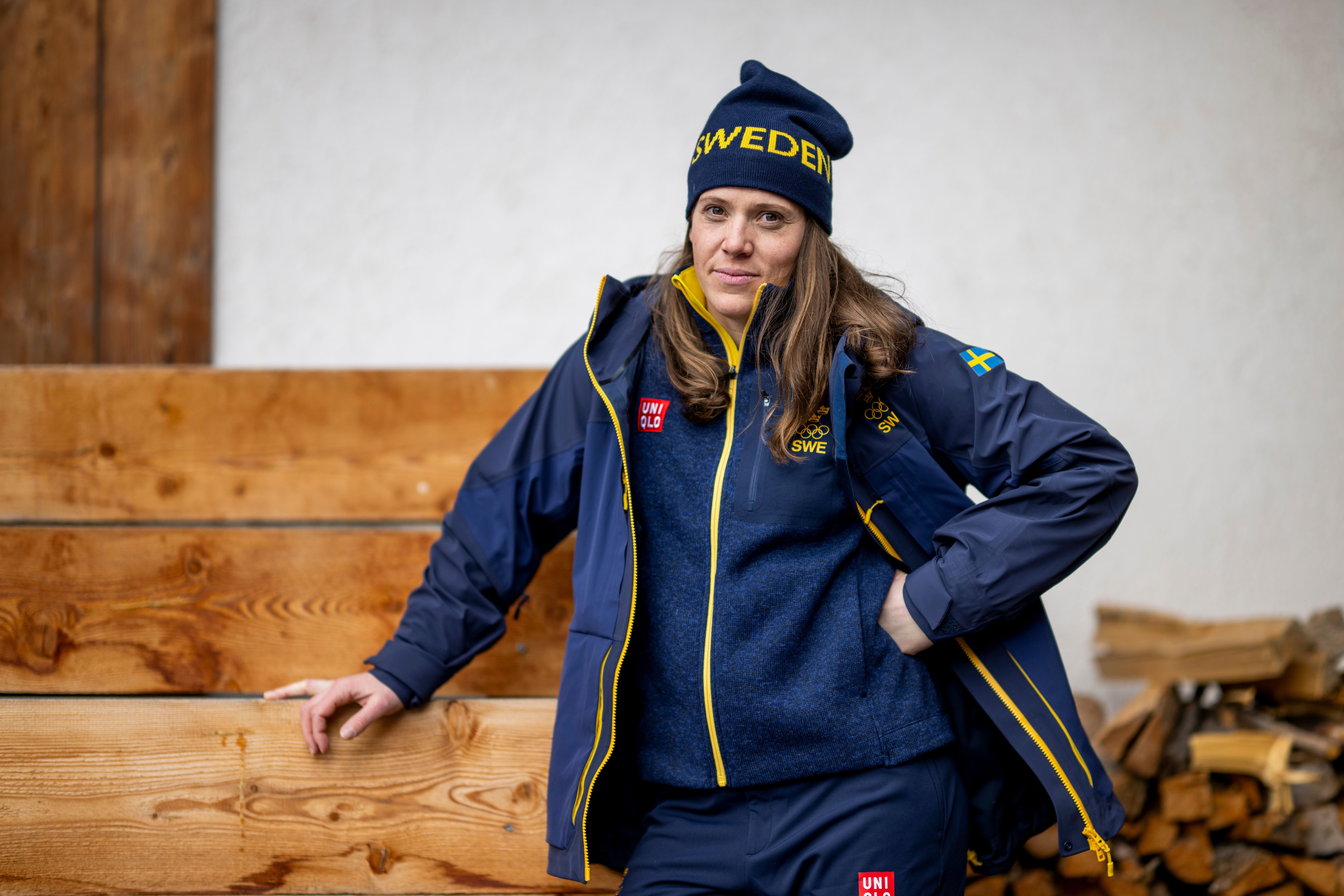 Eine Frau in schwedischer Teamkleidung steht entspannt vor einer Holzwand und sieht in die Kamera.