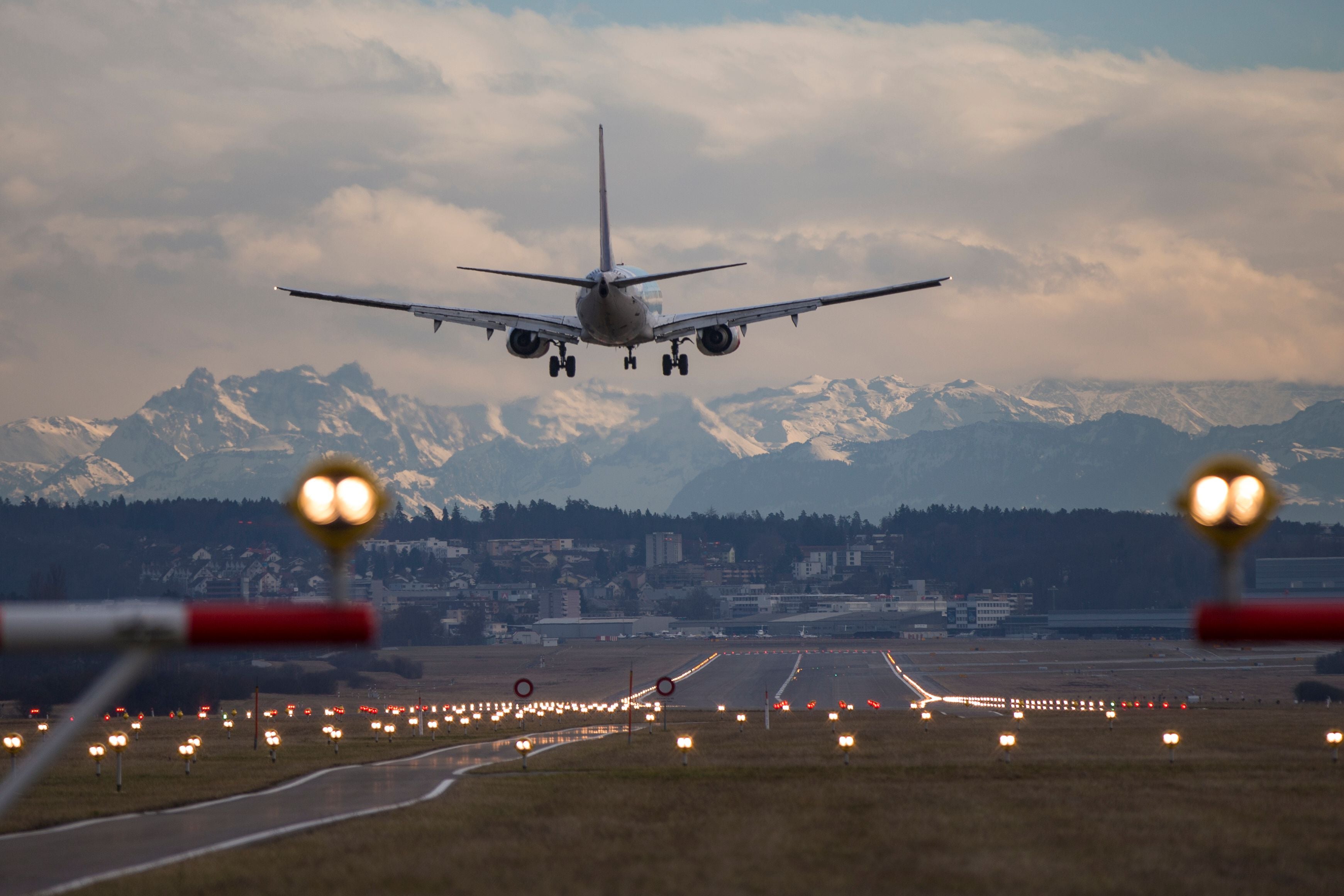 Flugzeug landet in Zürich vor Alpenkulisse und beleuchteter Landebahn.