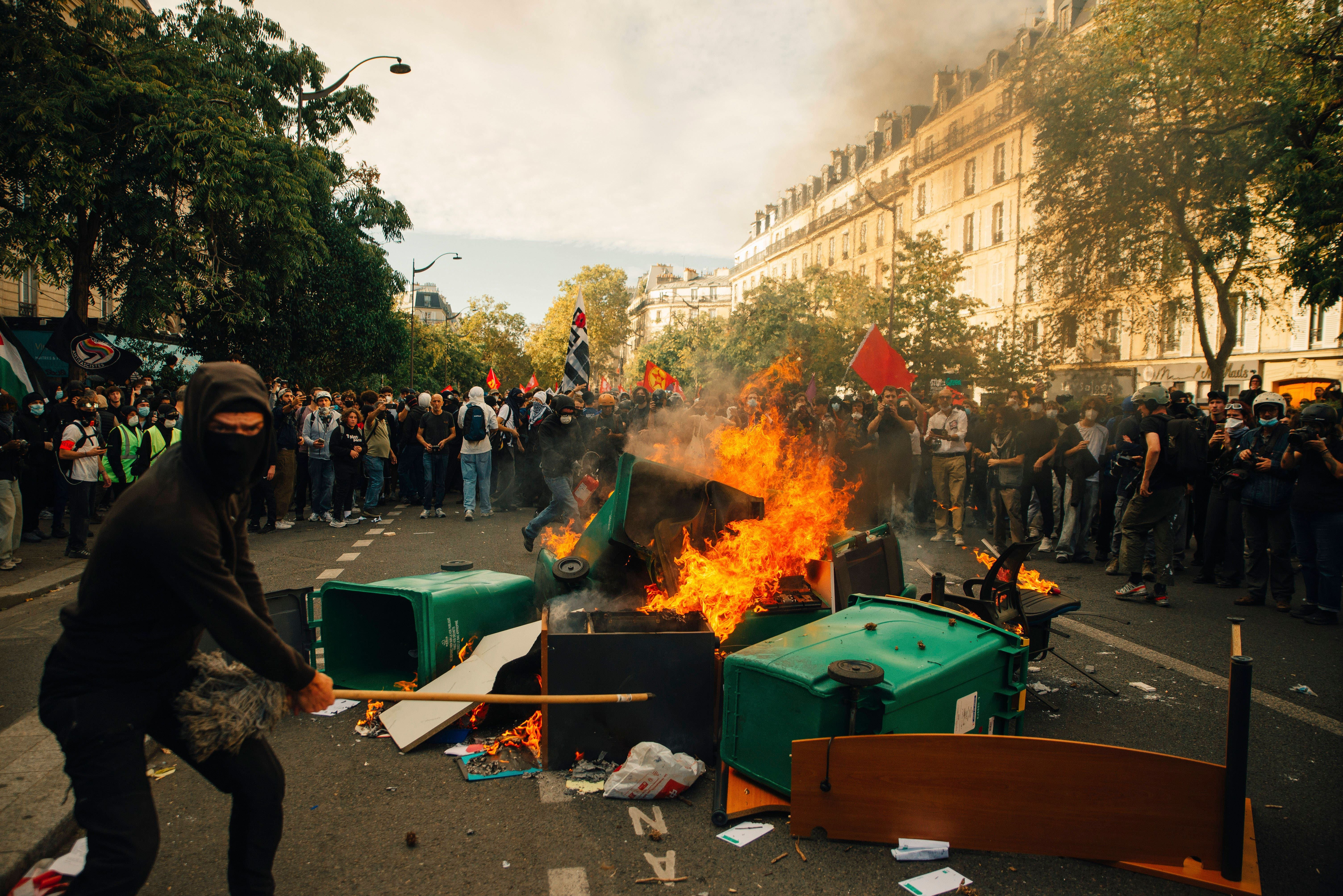 Demonstrant vor brennender Barrikade, umgeben von Protestierenden in einer Pariser Straße.