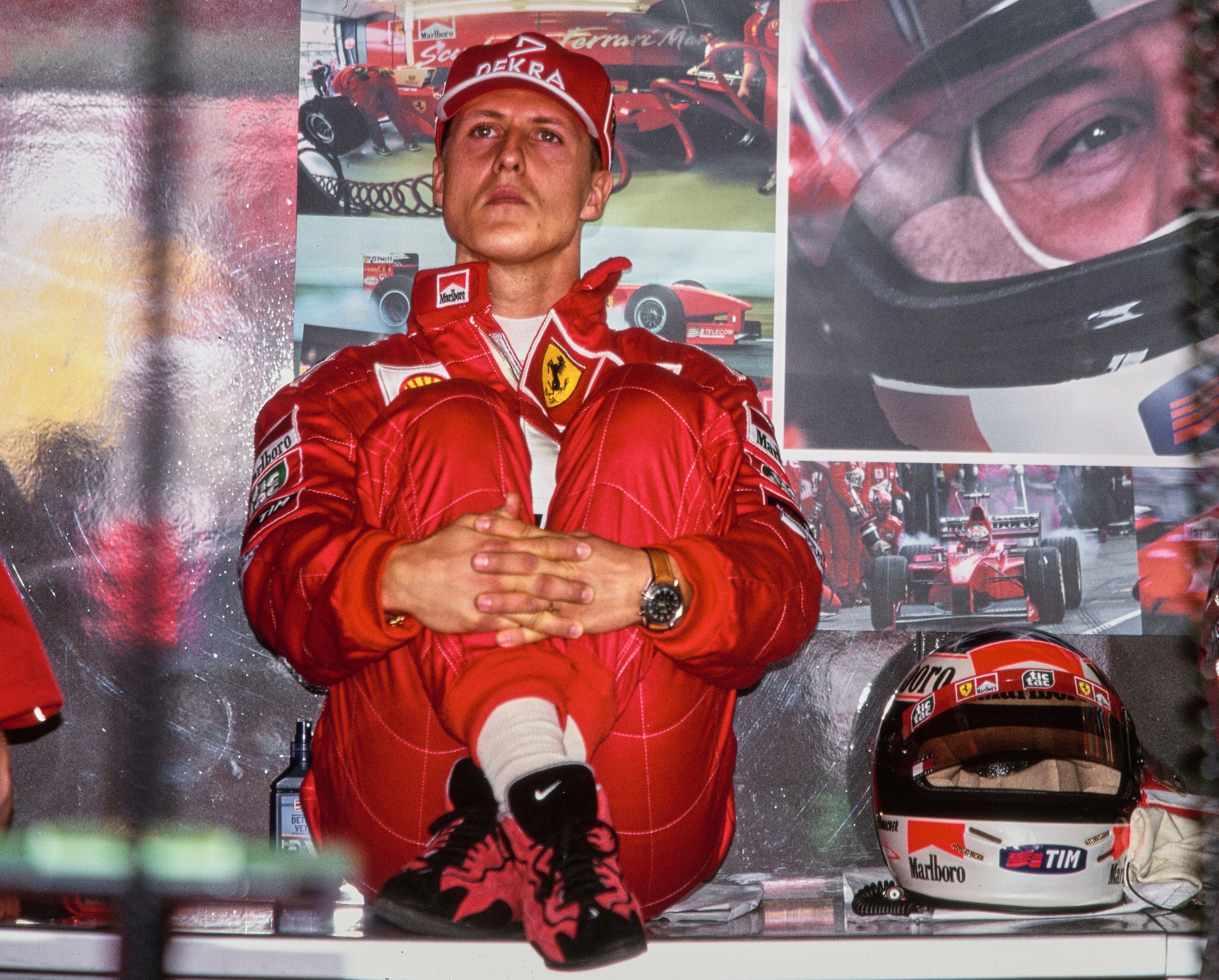 Formel-1-Fahrer im roten Ferrari-Overall sitzt nachdenklich in der Boxengasse, Helm steht daneben.