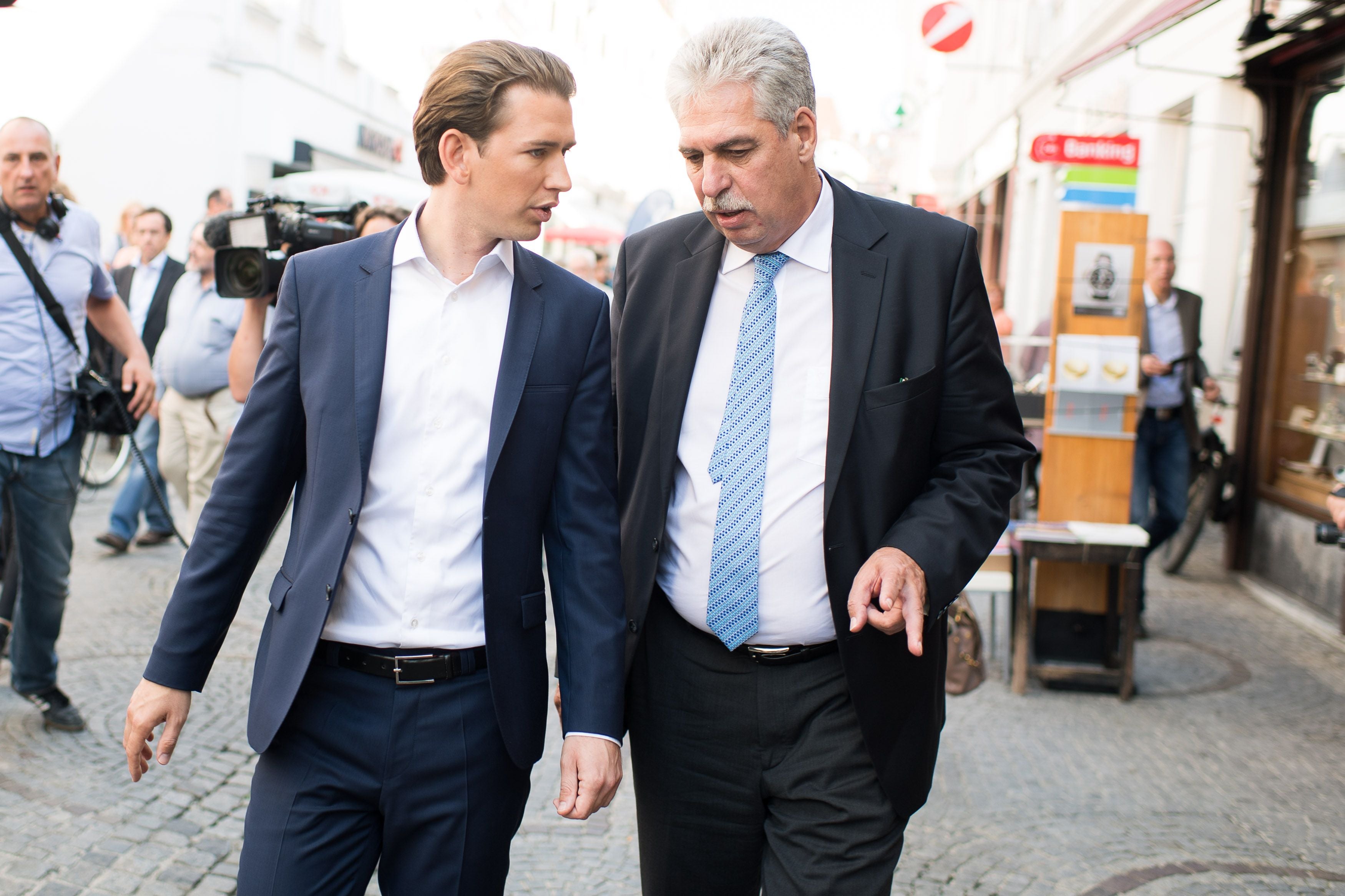 Zwei Männer im Anzug gehen und unterhalten sich auf einer belebten Straße in Wien.