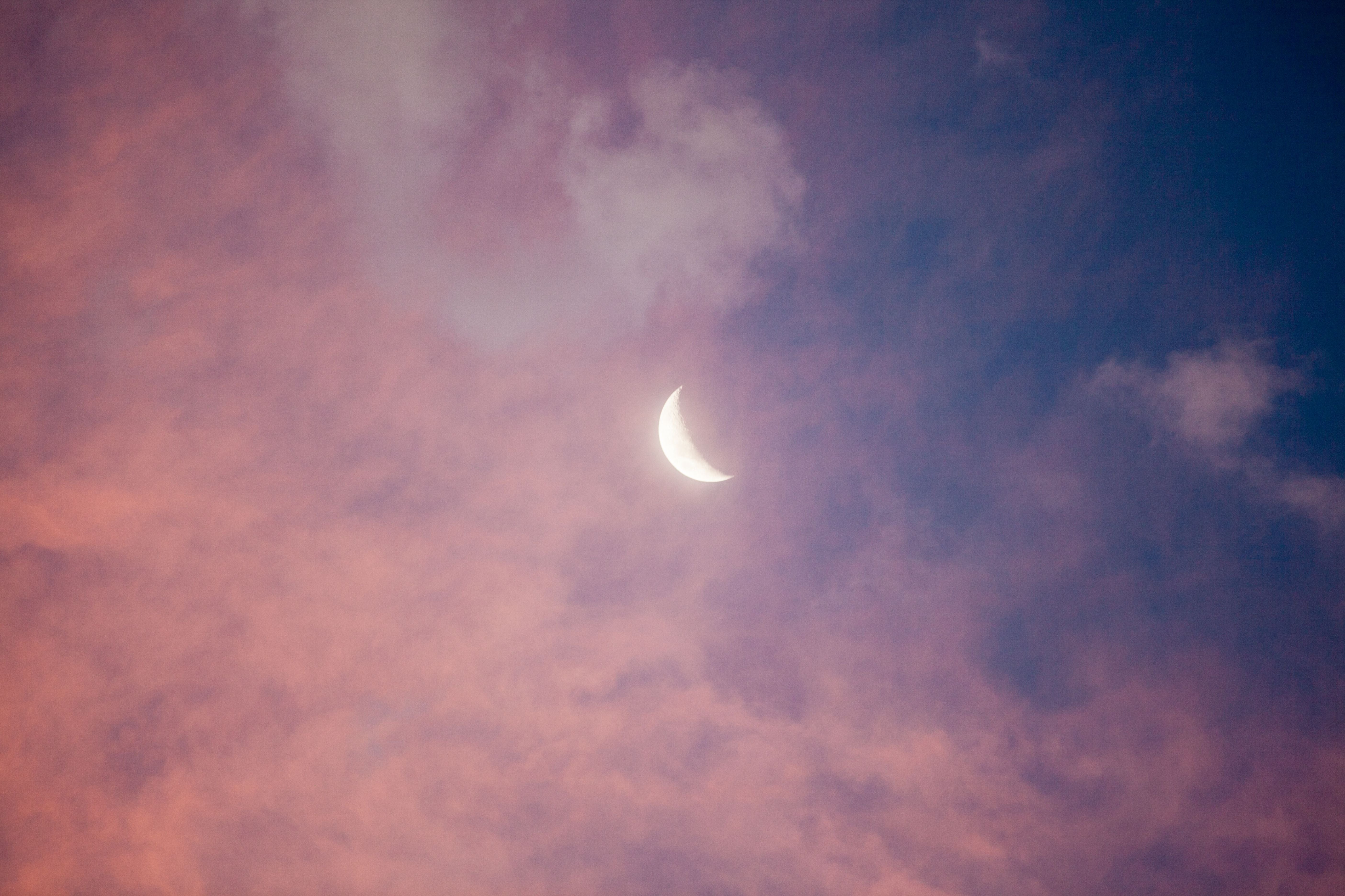 Sichelmond am Himmel mit rosa Wolken bei Sonnenuntergang.
