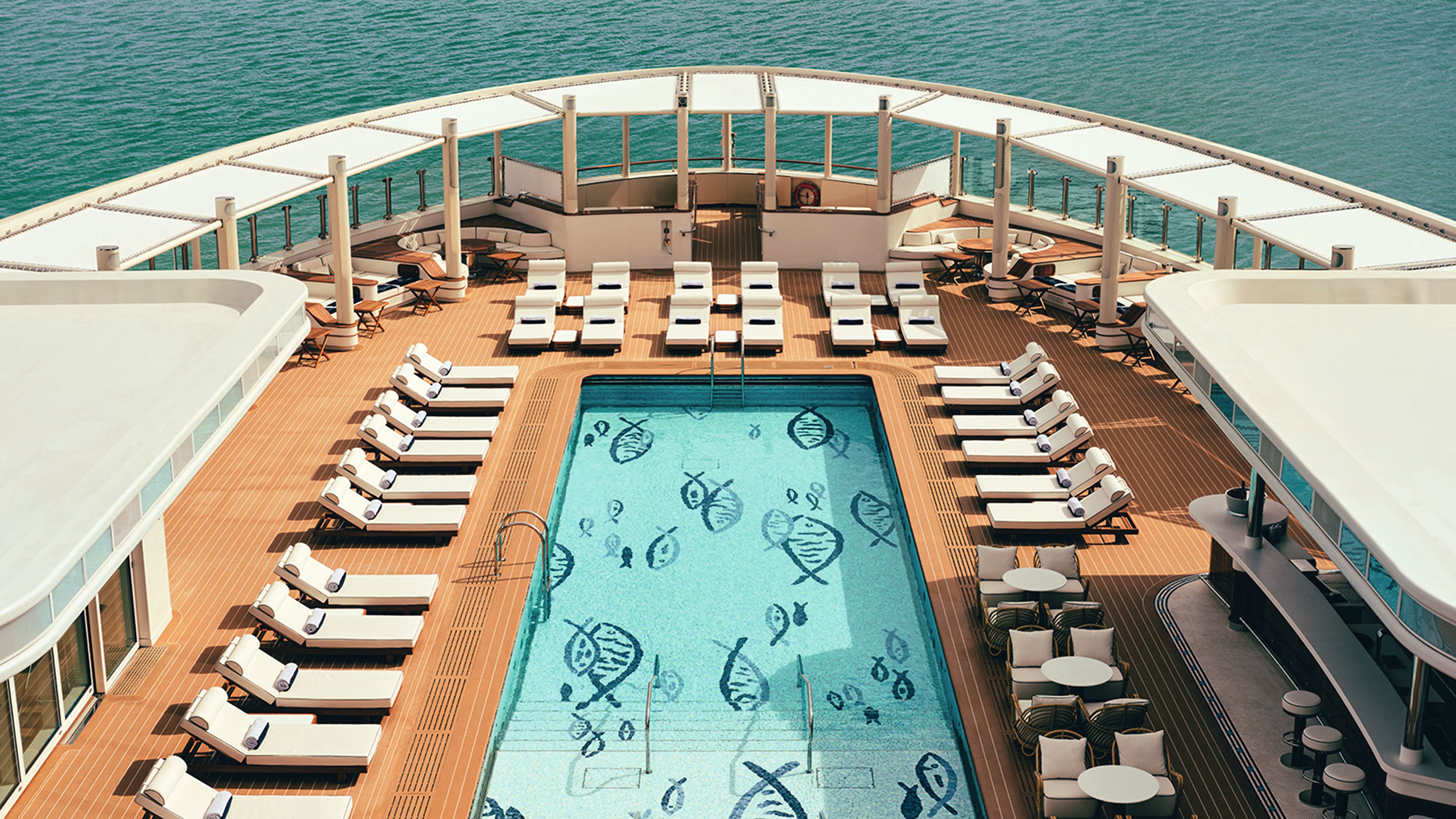 Sonnendeck eines Kreuzfahrtschiffs mit Pool, Liegen und Meer im Hintergrund.
