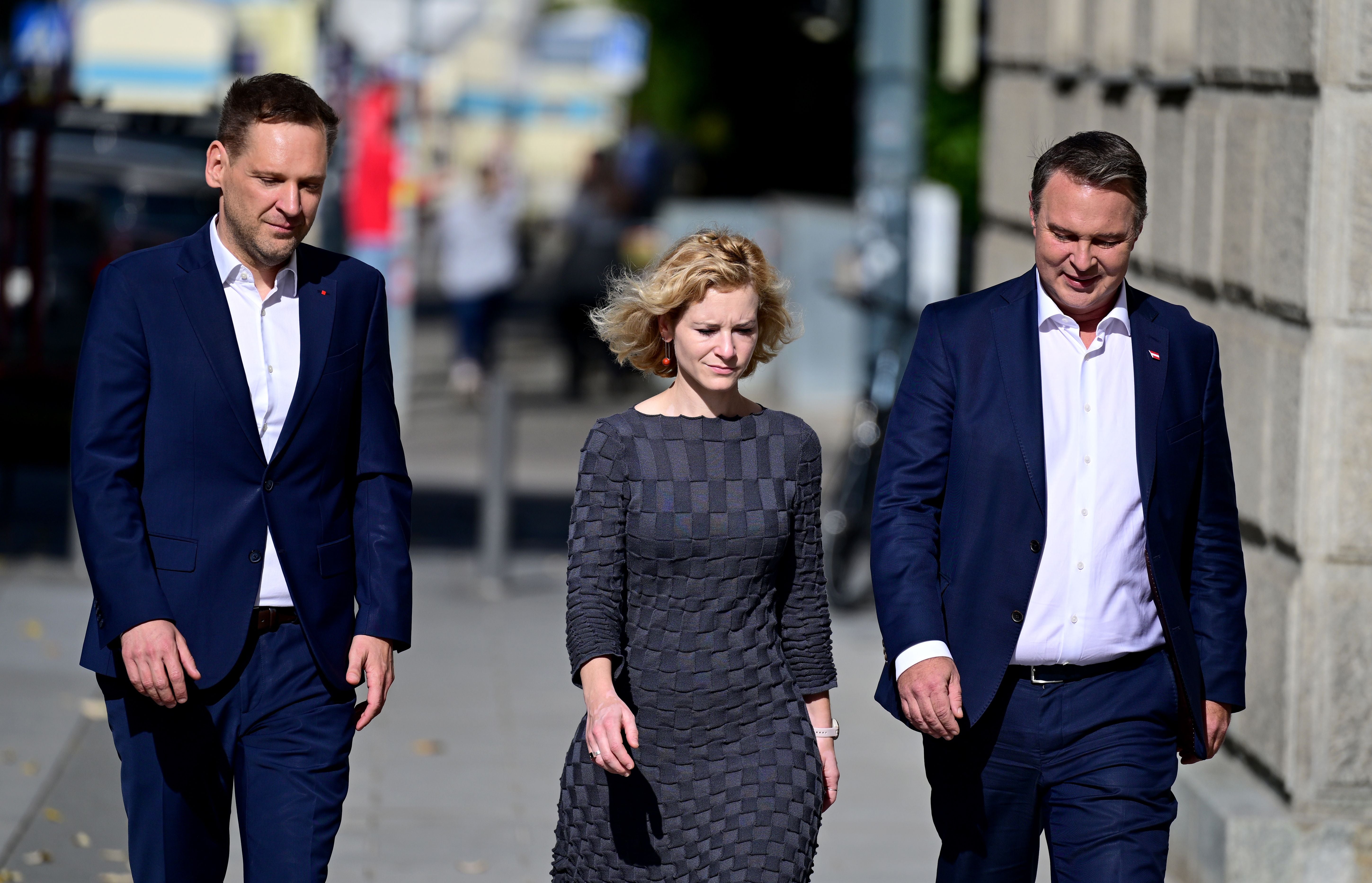 Drei Personen in Businesskleidung gehen nebeneinander auf einer Straße in Wien.