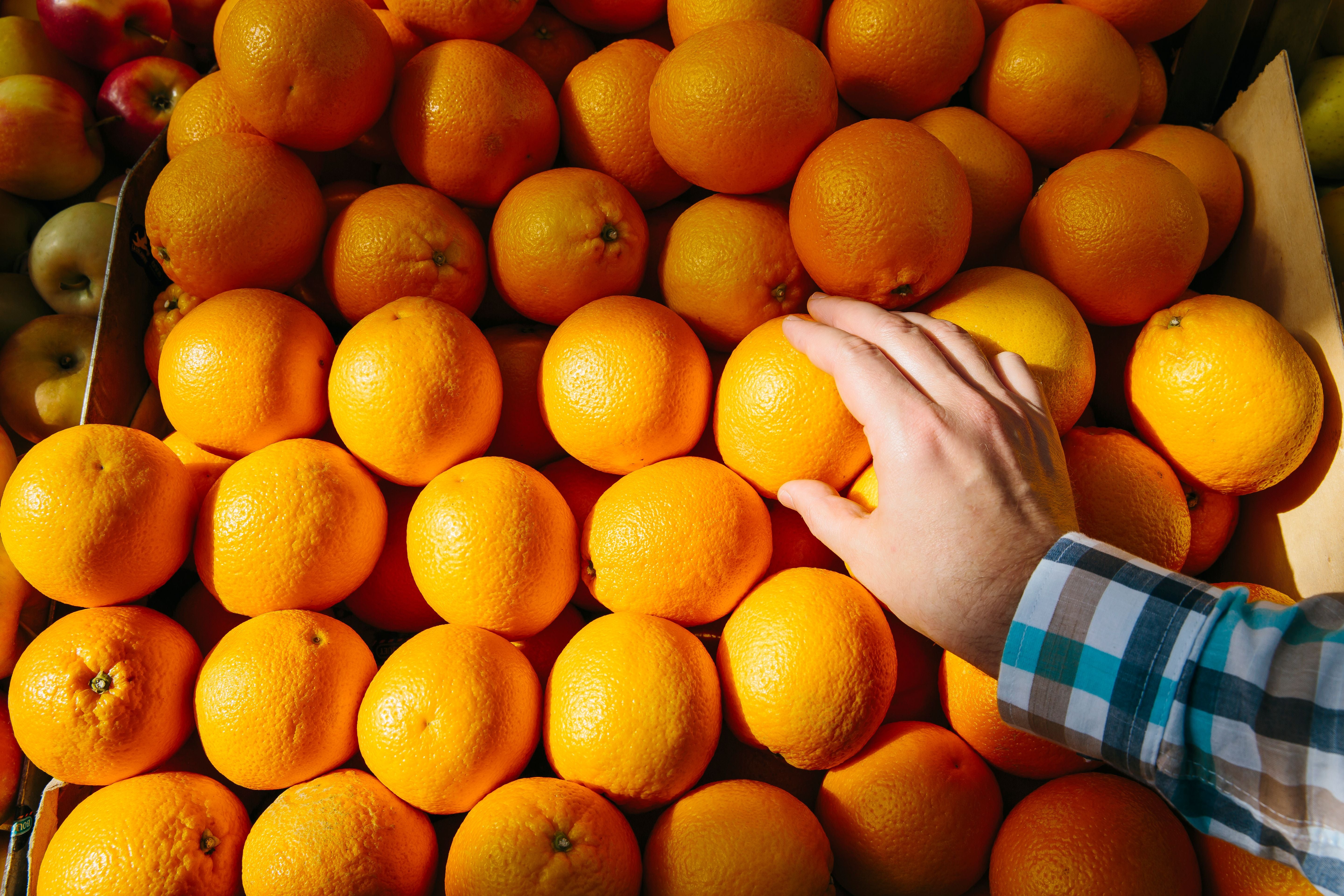 Eine Hand greift nach einer Orange auf einem Haufen frischer Orangen im Supermarkt.