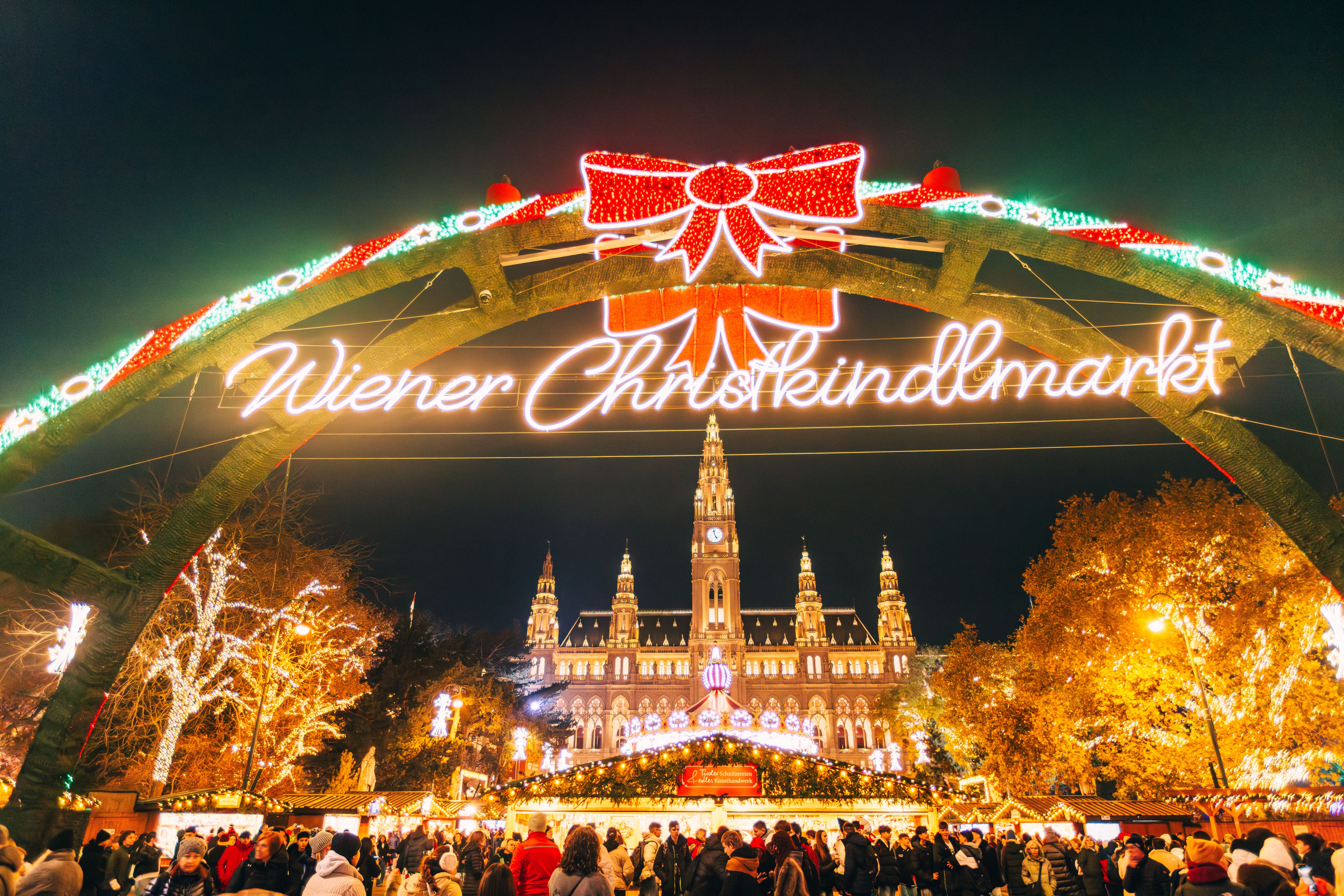 Beleuchteter Eingang zum Wiener Christkindlmarkt am Rathausplatz mit festlichem Treiben bei Nacht.